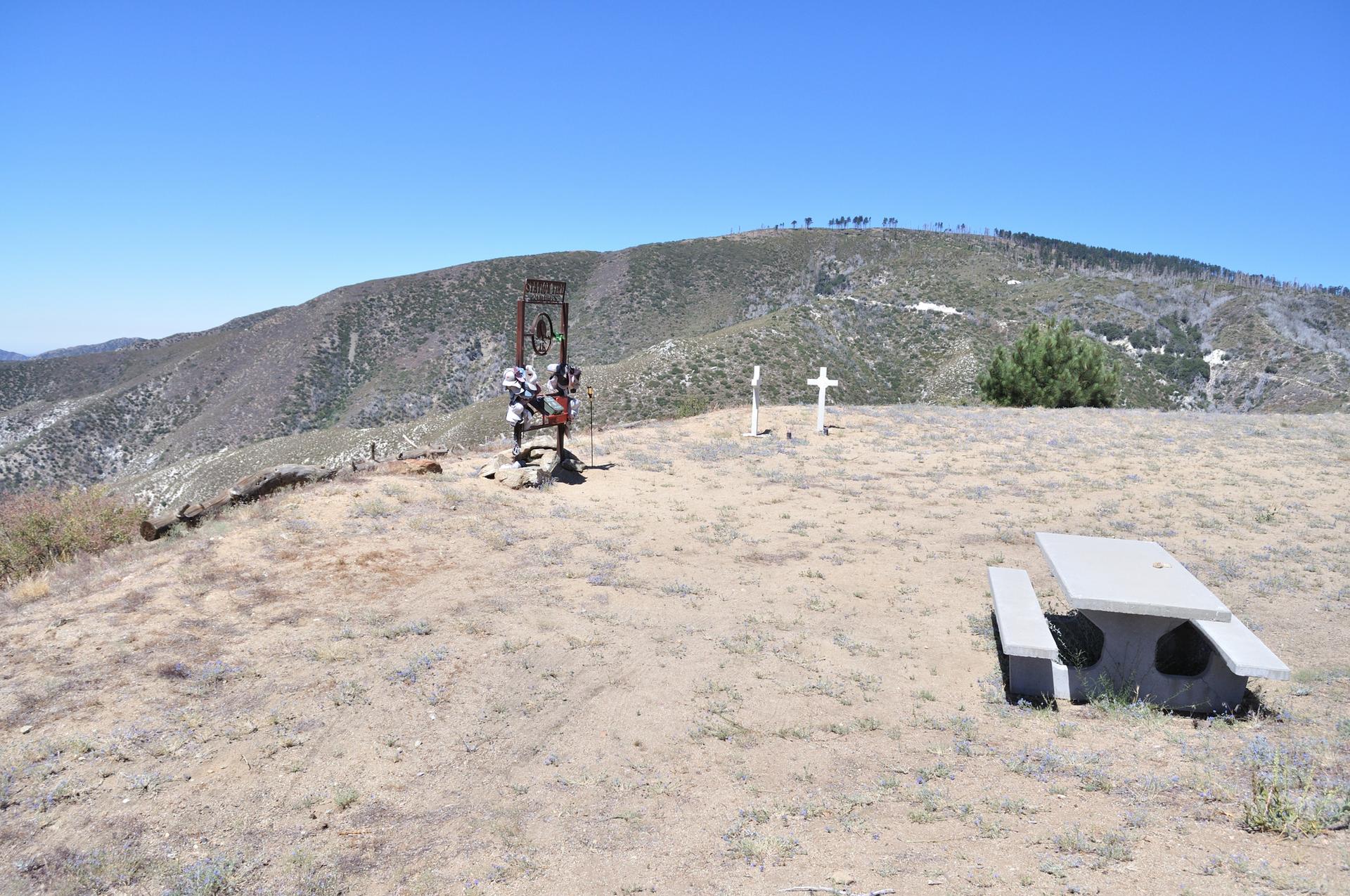 Picnic table and memorial crosses on a barren hilltop with distant mountains.