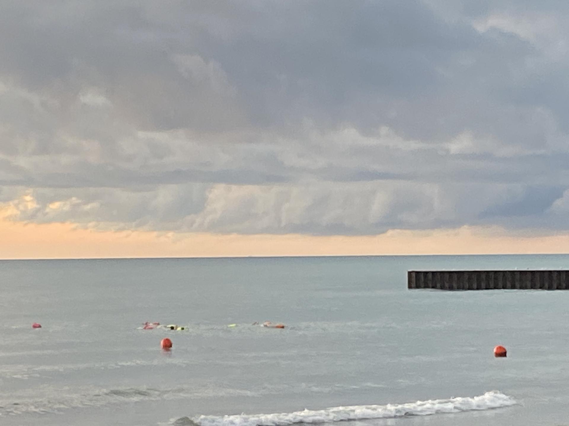 Choppy water with orange buoys and a distant pier under a cloudy sky.