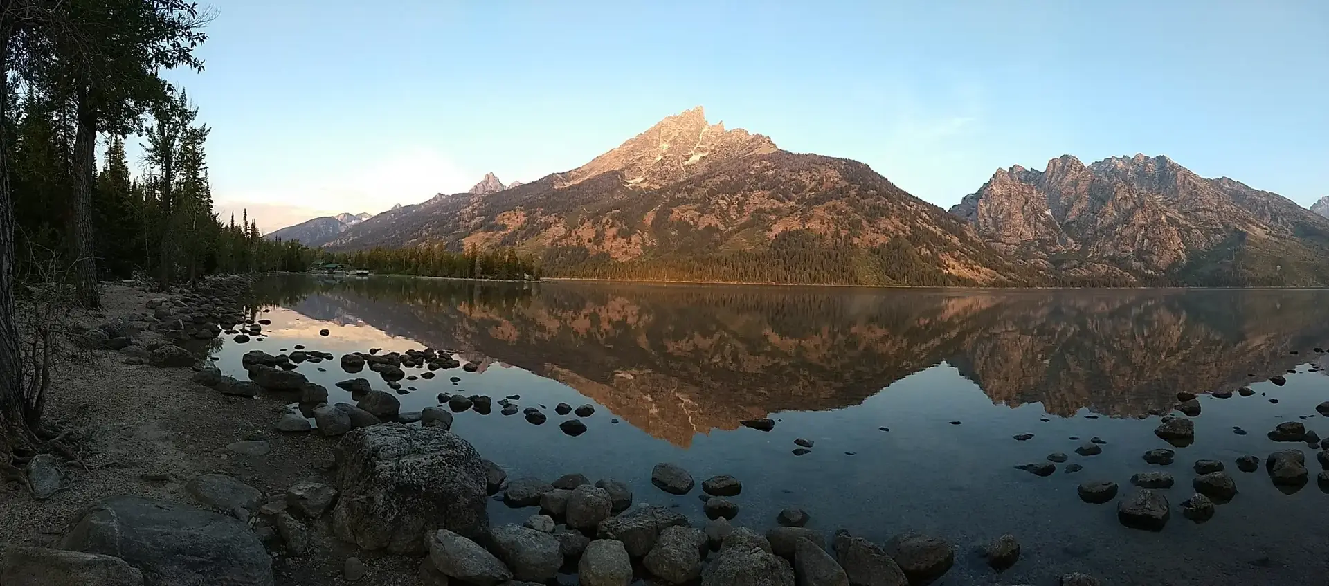 A large mountain reflects perfectly in a calm lake during golden hour light.