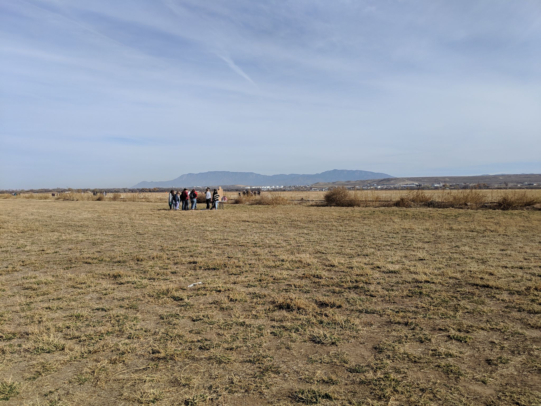 A group of people stand in a vast, dry field under a clear sky. - Paseo del Bosque Trail