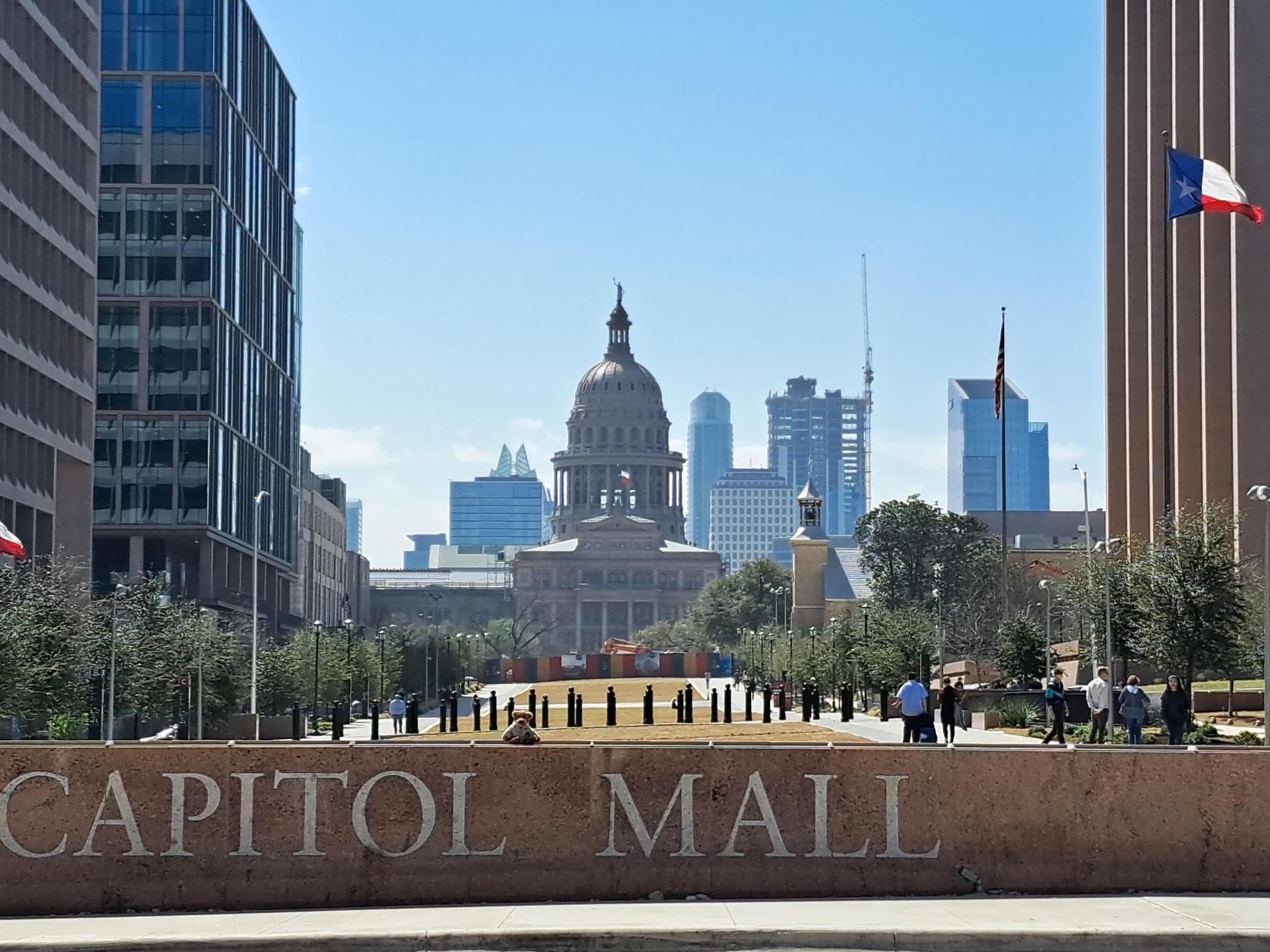 Domed building framed by modern towers, with people walking on a sunny day.