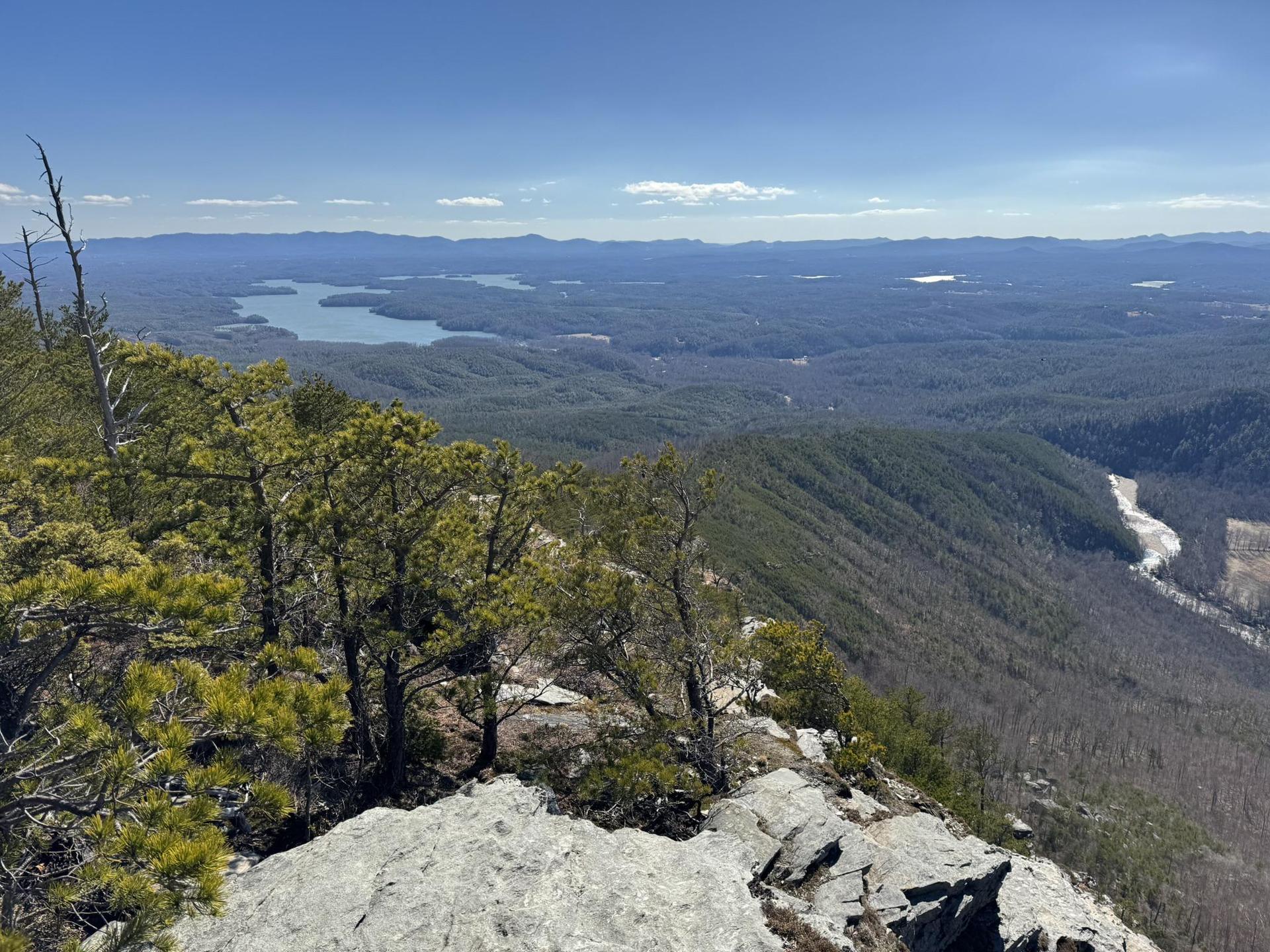 Panoramic view from a mountain peak, showing a lake and distant hills.