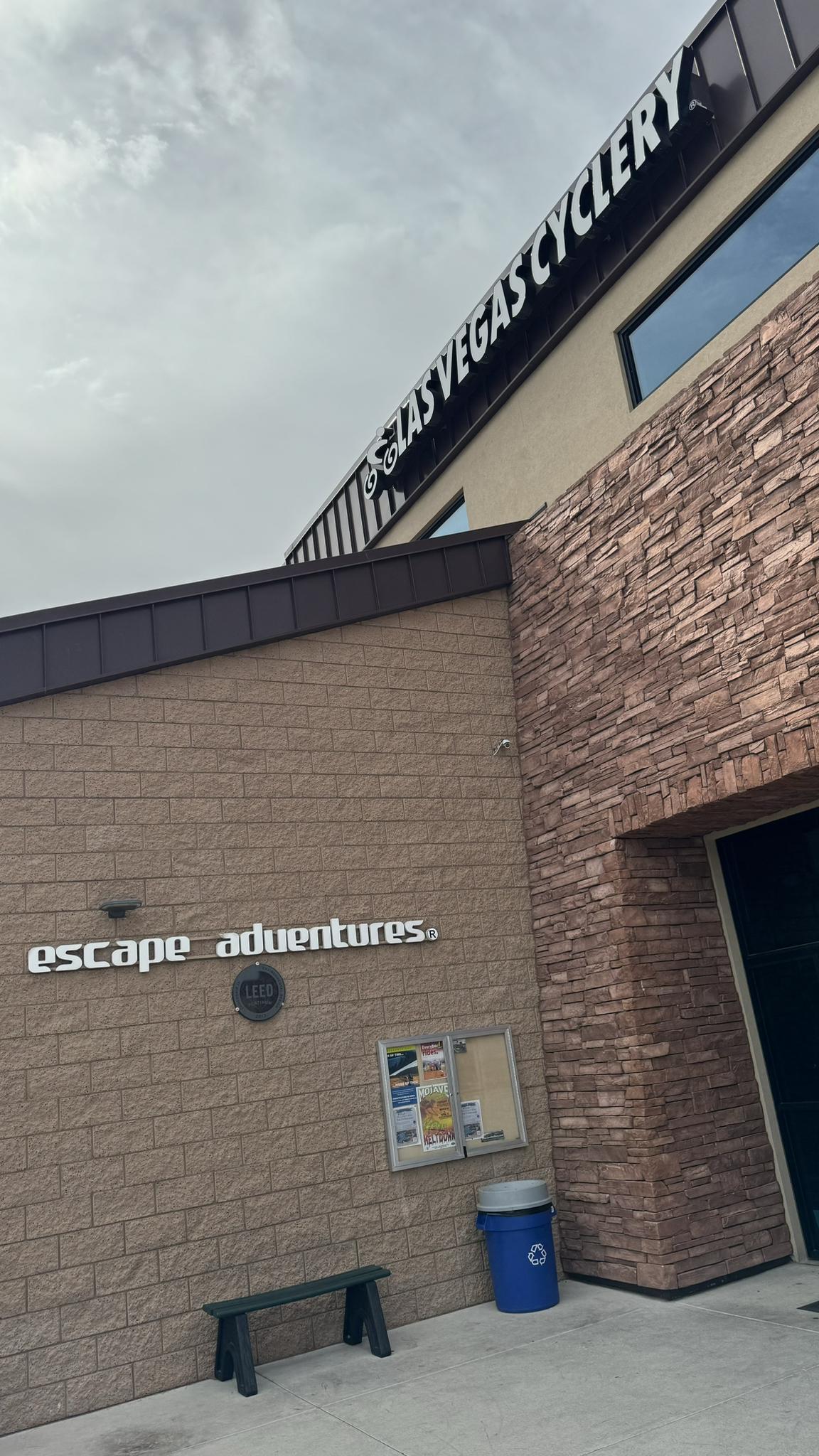 Building exterior with brick walls, signs, a bench, and a trash can under cloudy sky.