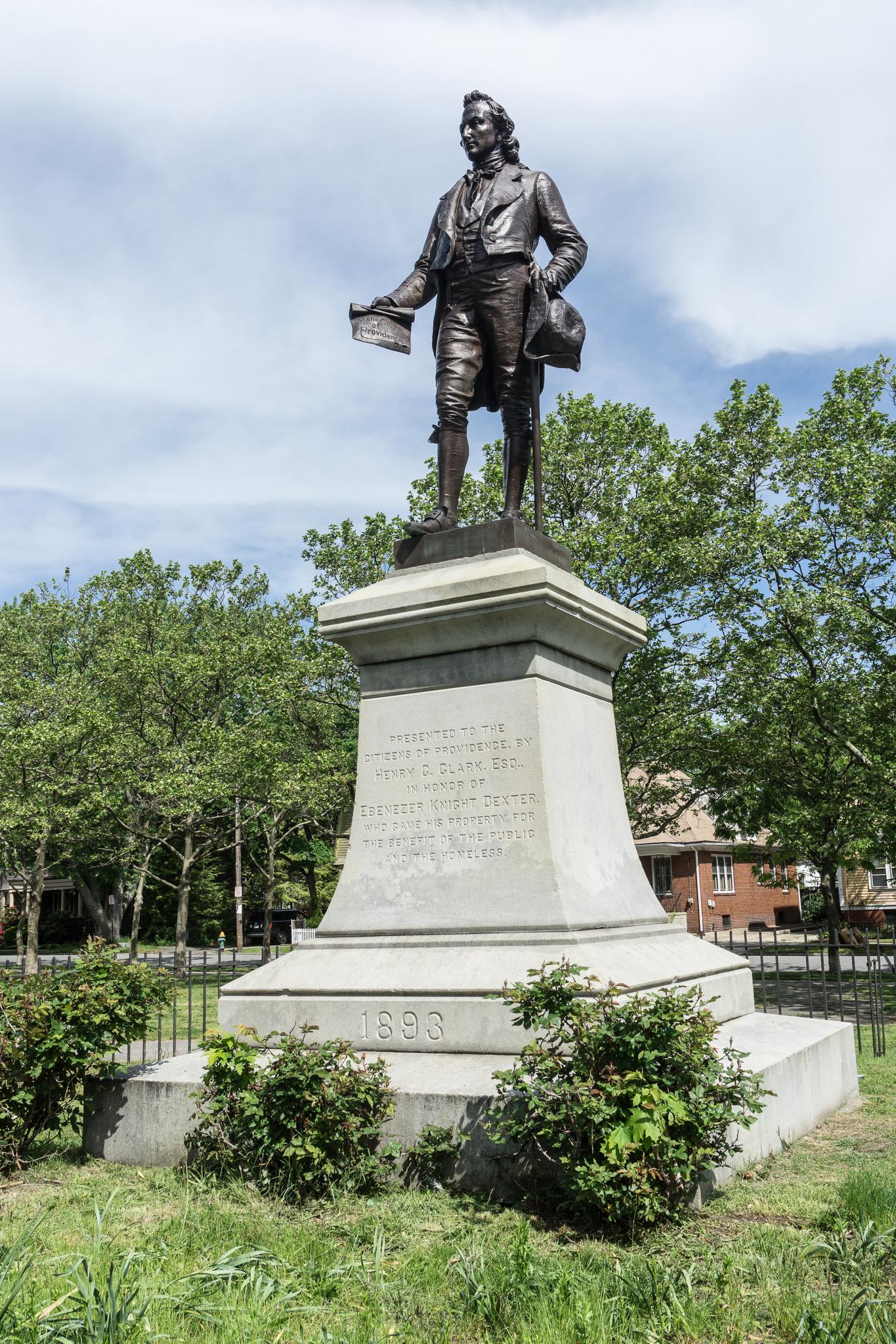 Bronze statue of a man on a stone pedestal surrounded by green trees.