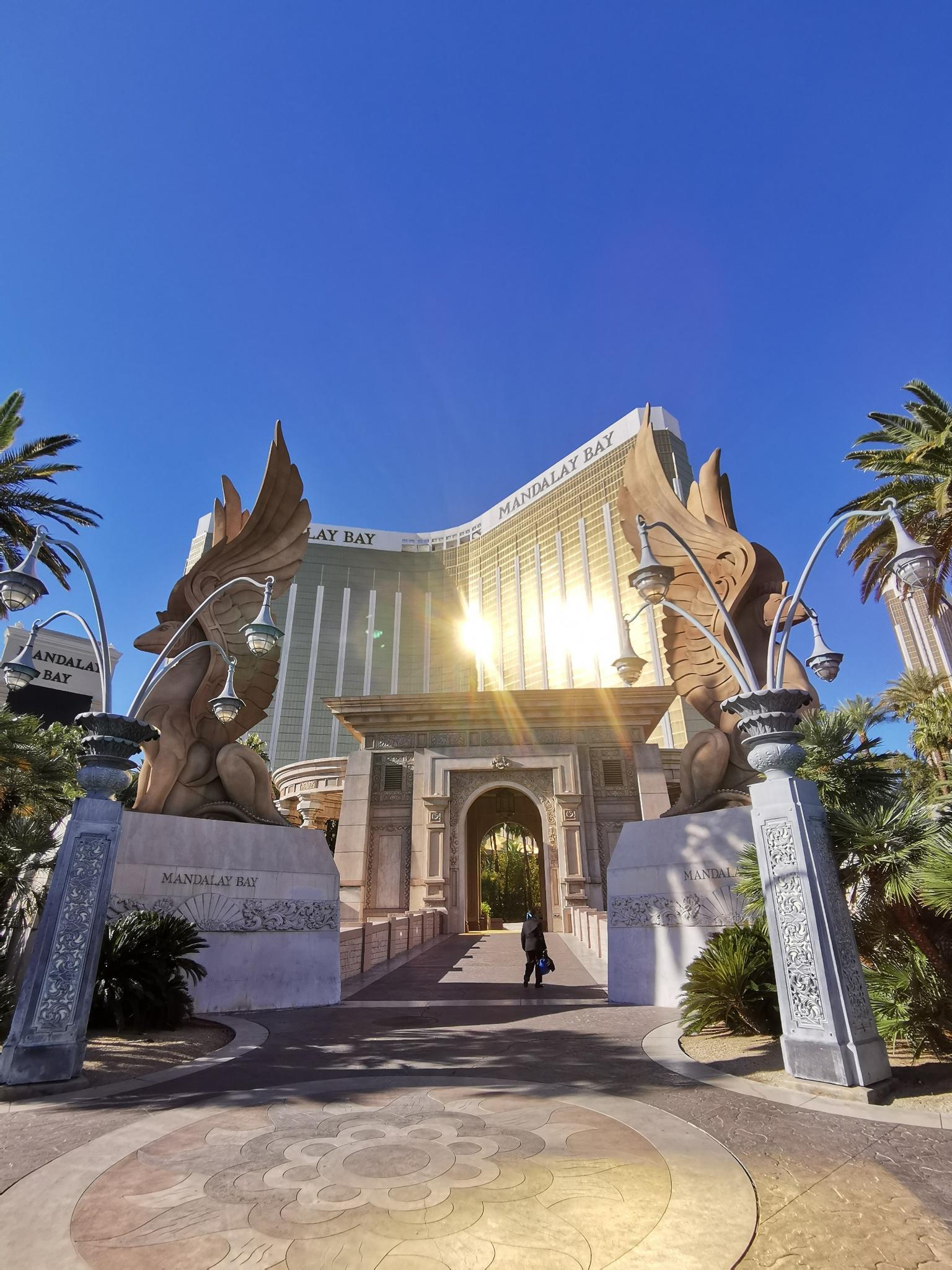 Grand building entrance with large statues, sun glare, and a person walking.