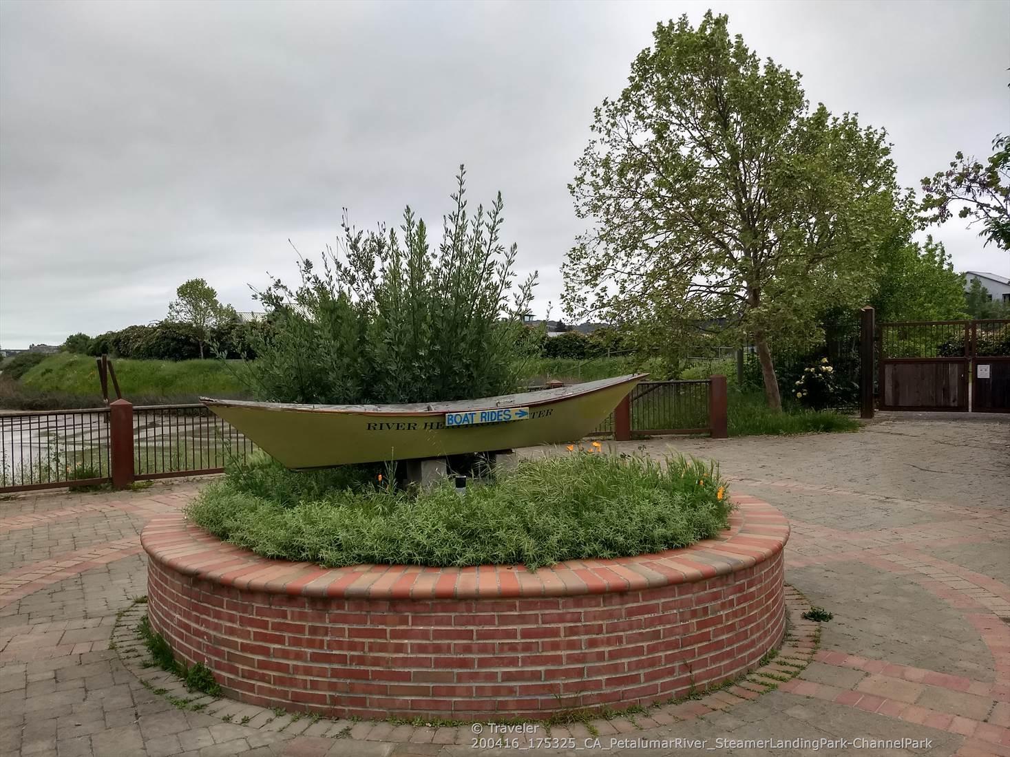 A decorative boat in a brick planter on a paved area under a cloudy sky.