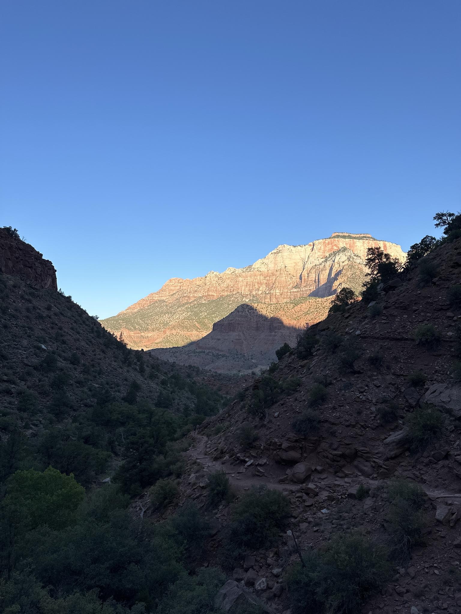 Sunlight illuminates a distant mountain peak, casting long shadows over a dark canyon.