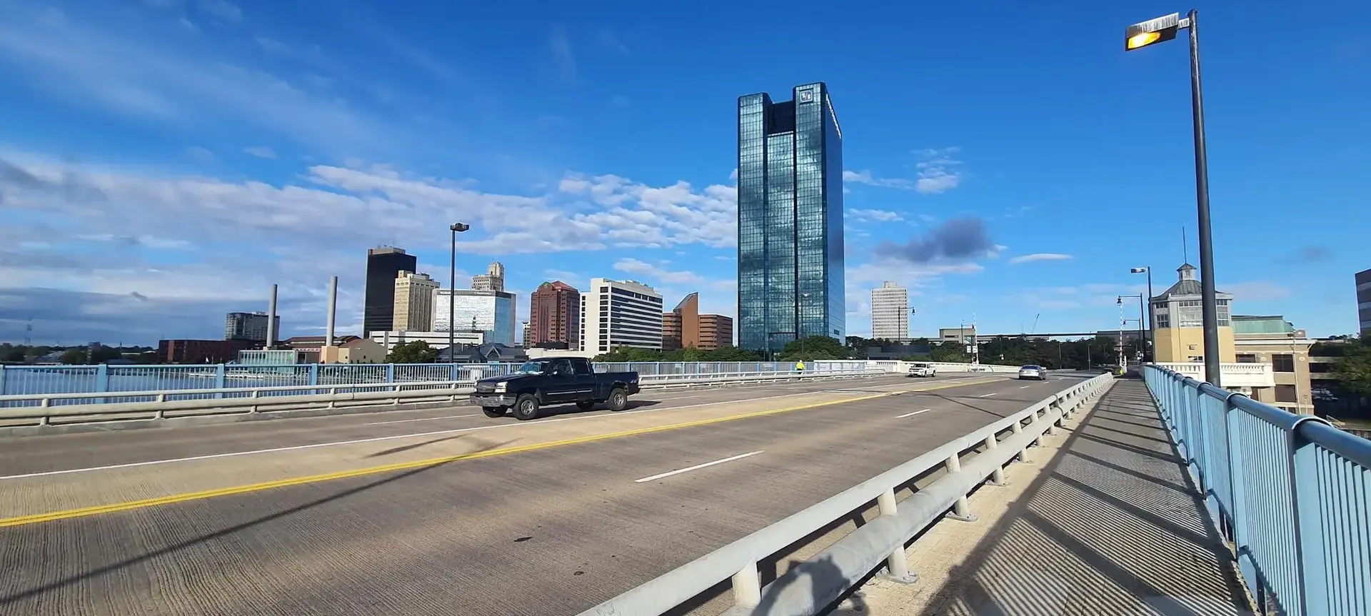 Cars on a bridge with a city skyline under a bright blue sky.
