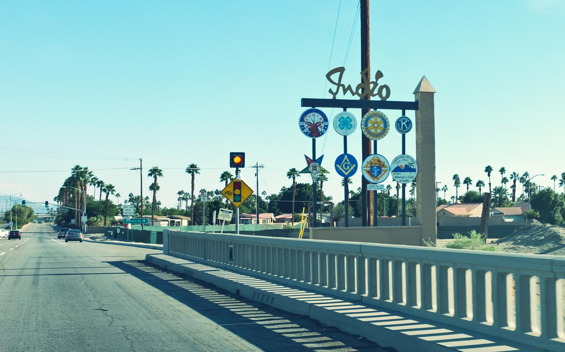 Road leading to a sign with symbols, lined by palm trees.