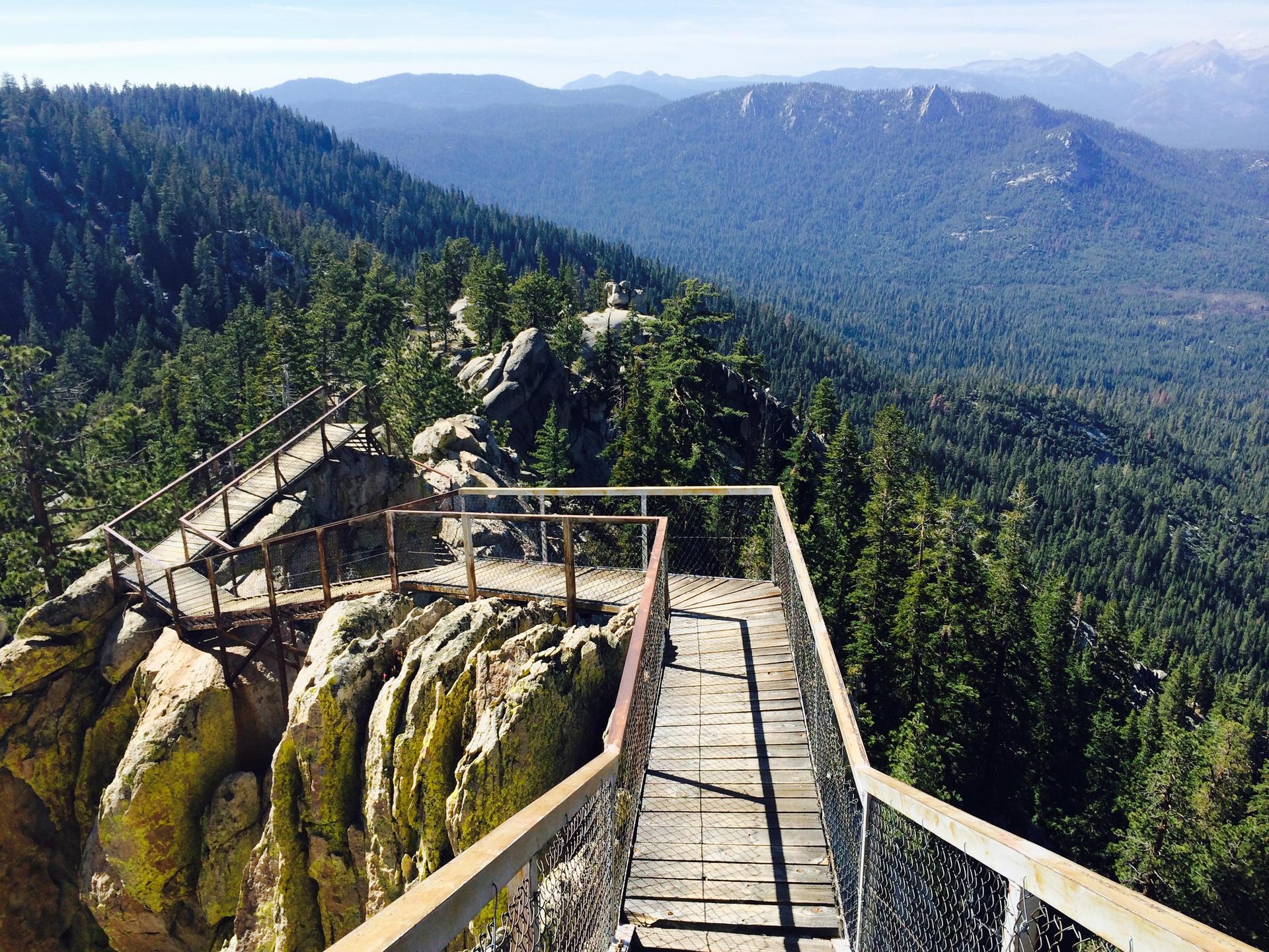 Wooden boardwalks and stairs wind around rocky cliffs overlooking a vast forest.