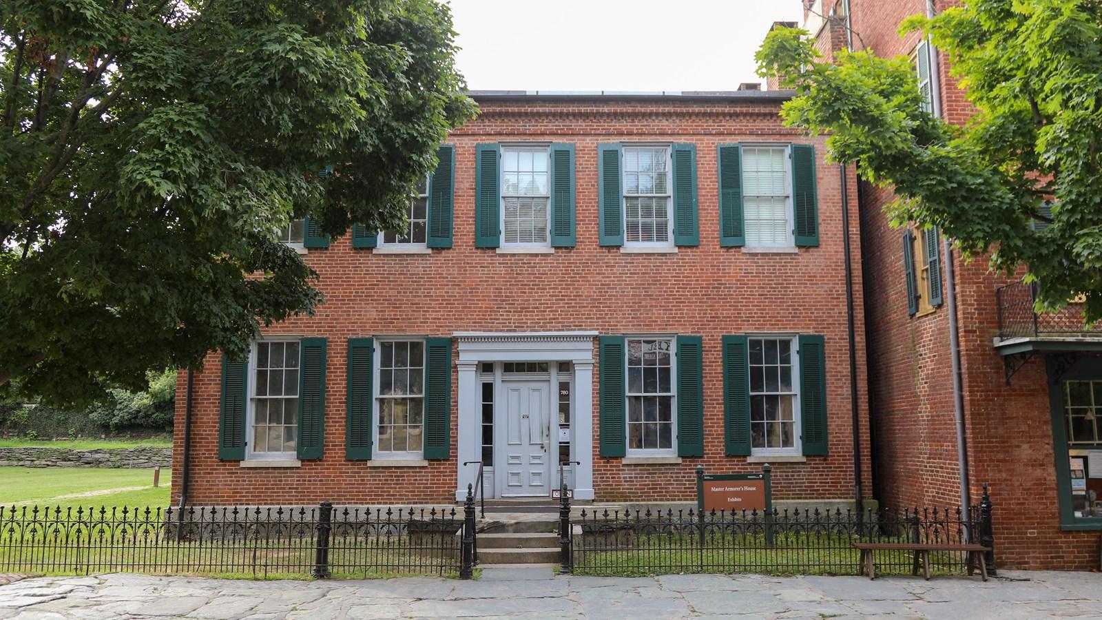 A red brick building with green shutters and white trim, surrounded by trees.