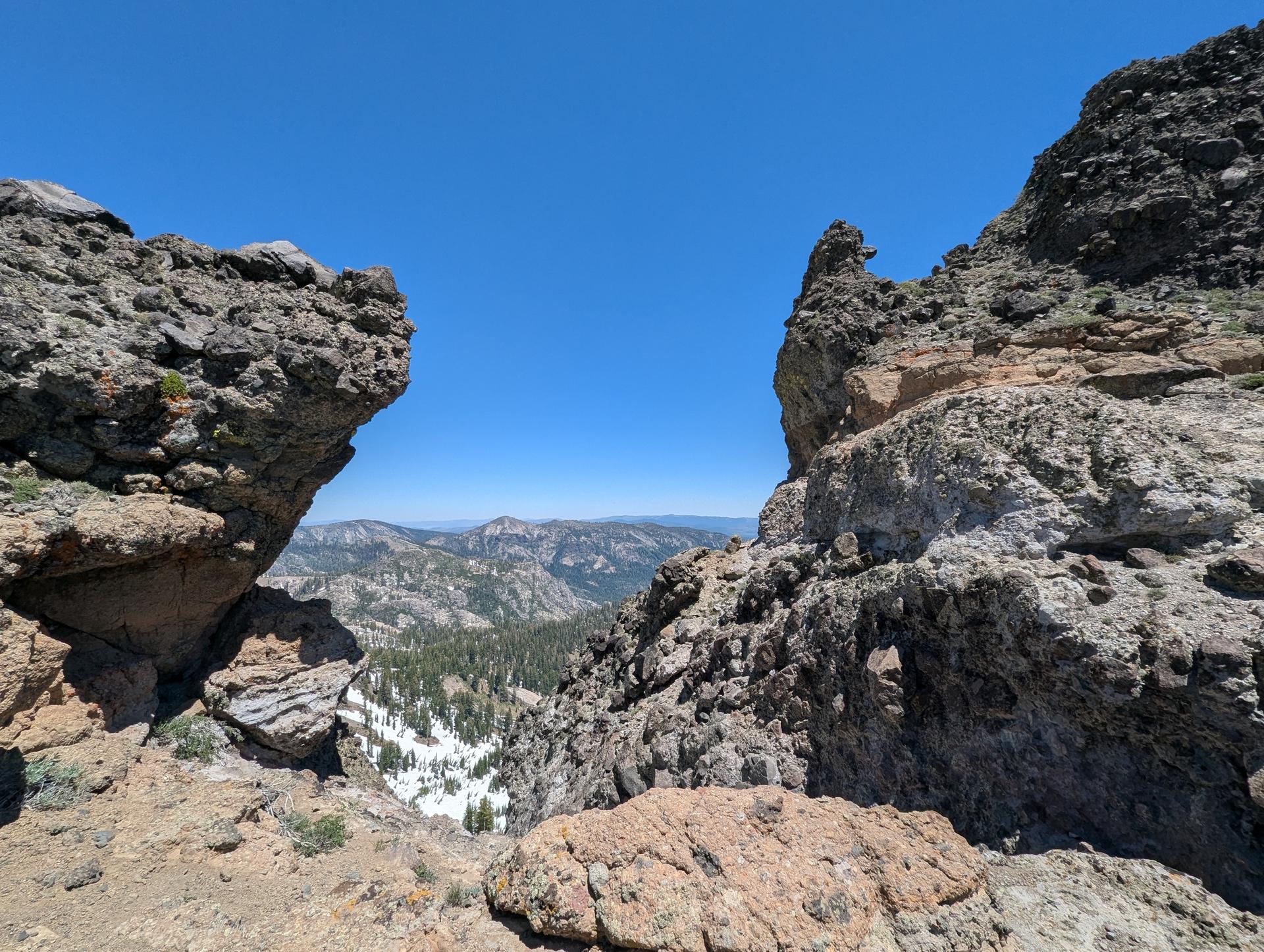 Rocky mountain pass overlooking a valley with snow patches.