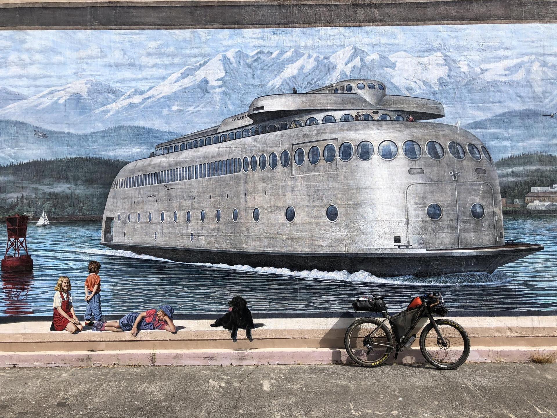 Colorful mural of a large ferry and mountains, with a bicycle parked nearby.