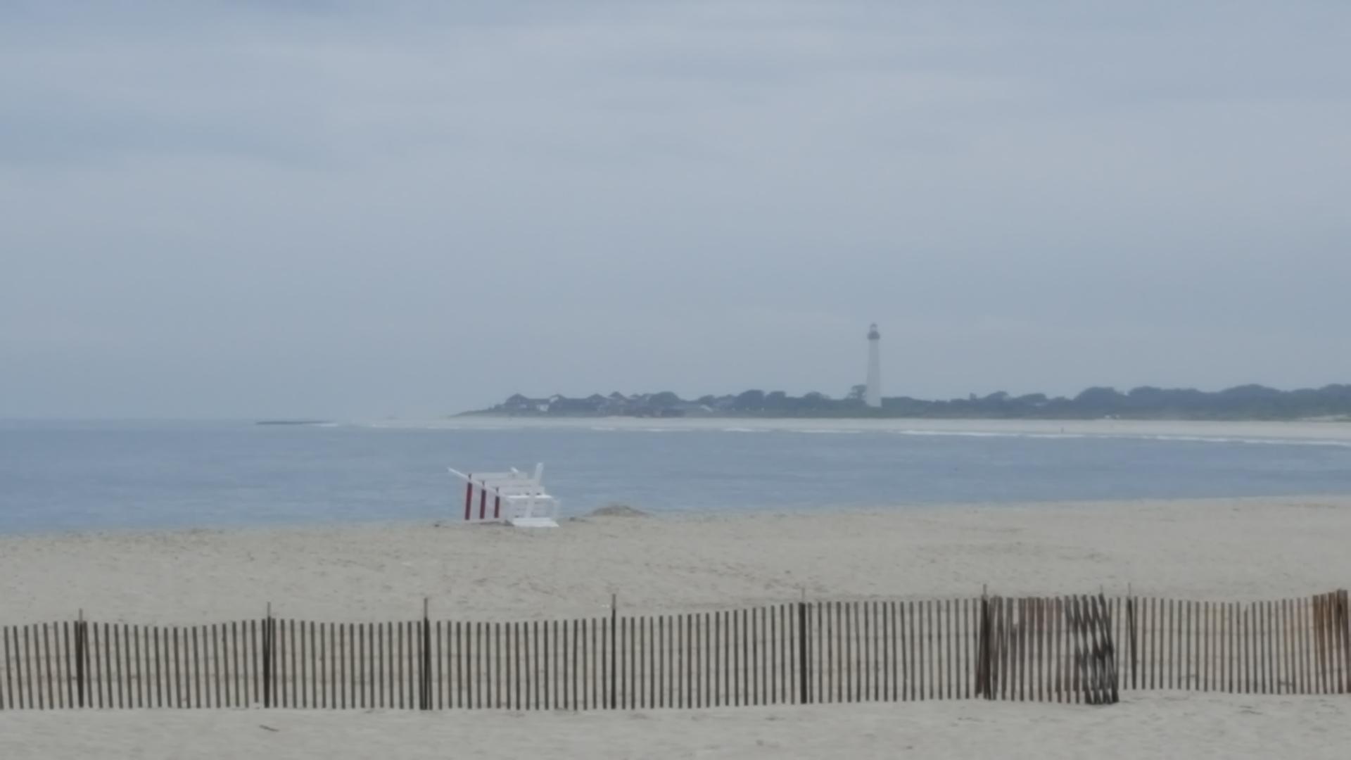 Hazy beach scene with a lifeguard chair, ocean, and distant lighthouse.