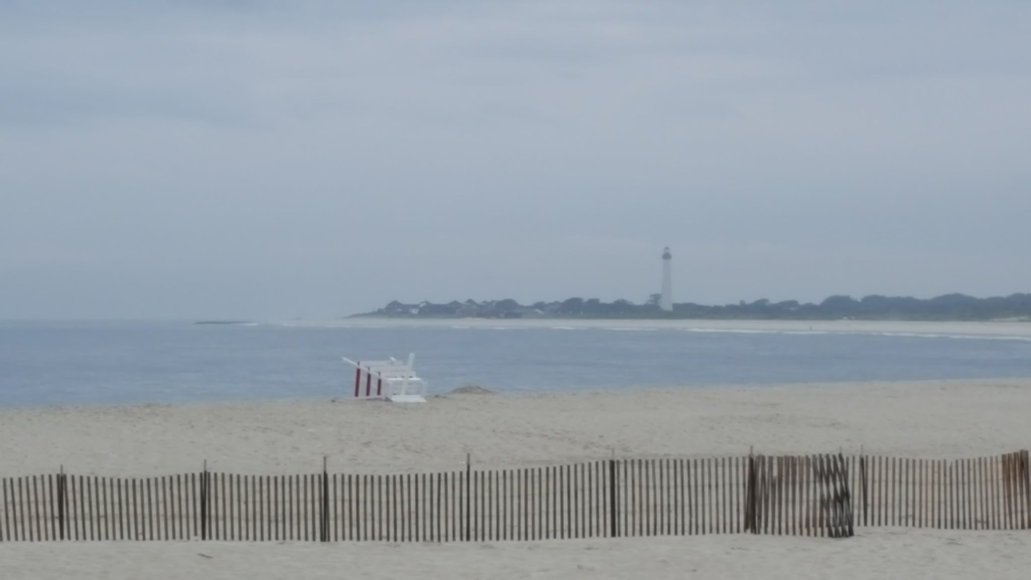 Hazy beach scene with a lifeguard chair, ocean, and distant lighthouse. - Second Ave Beach – Cape May Beach loop from Cape May