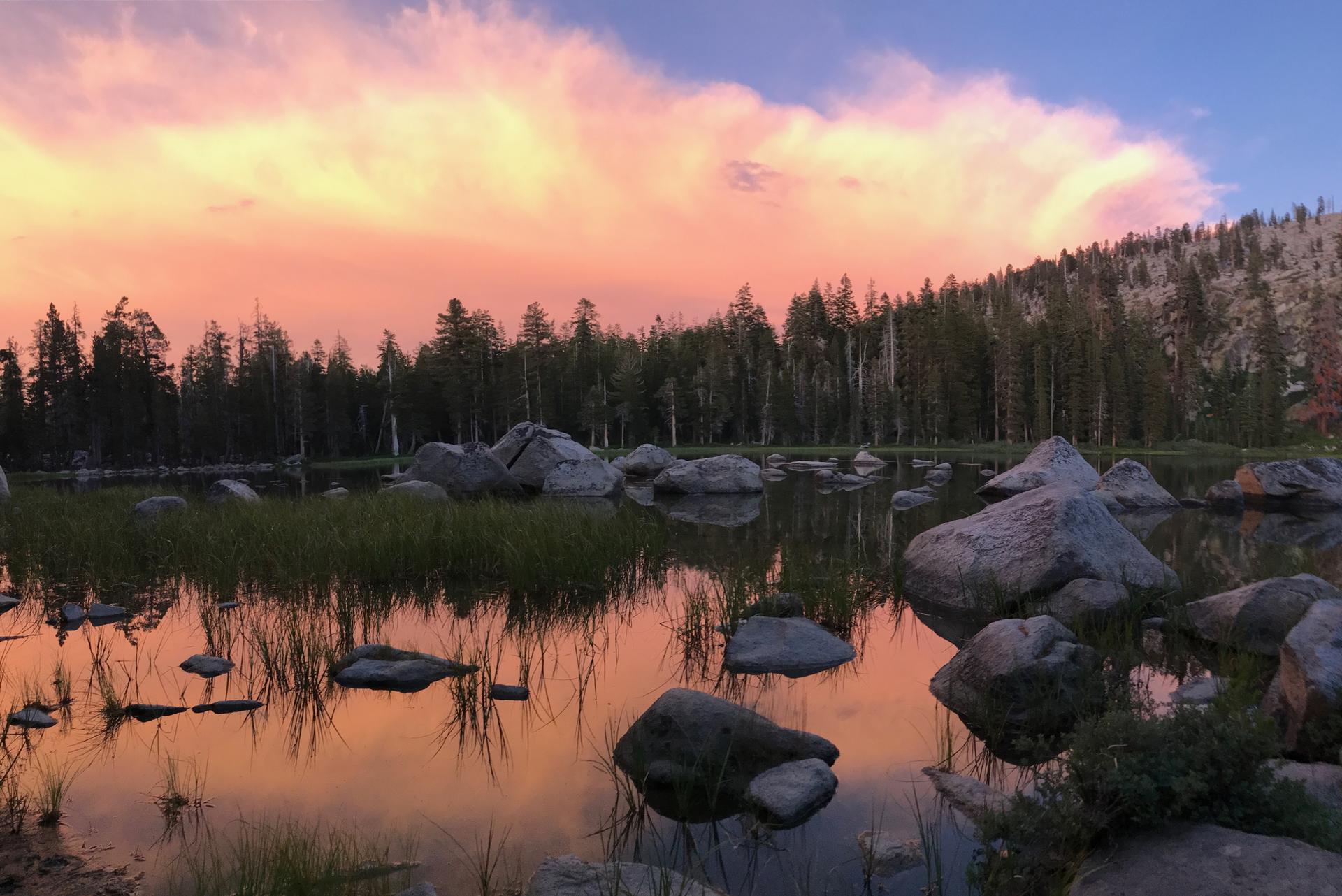 Vibrant sunset over a rocky lake, reflecting colorful clouds and trees.