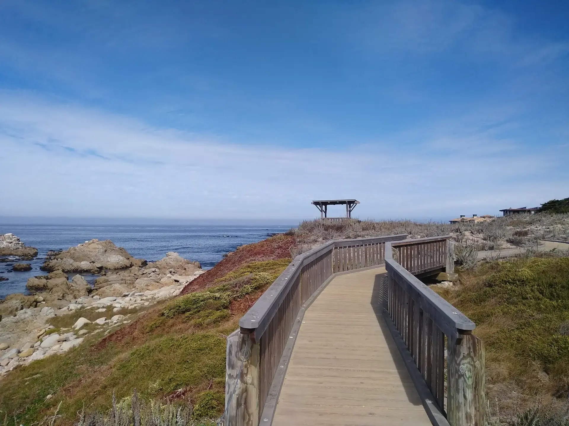 Wooden boardwalk overlooking a rocky coastline and calm blue ocean.
