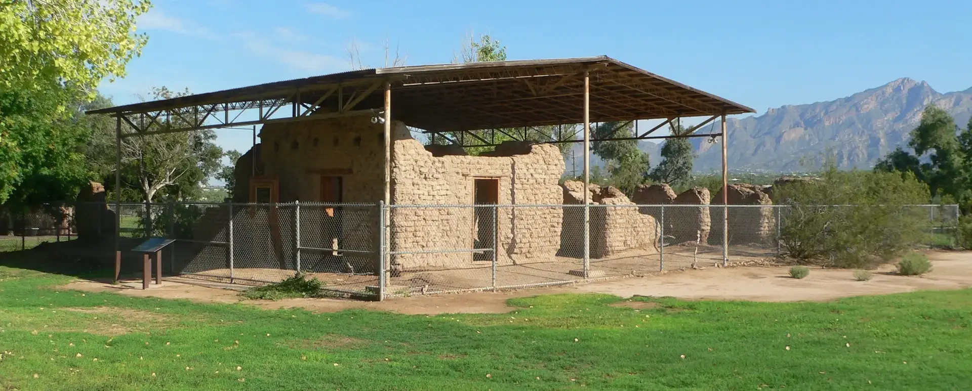 Ancient stone ruins under a modern protective roof on a bright, sunny day.