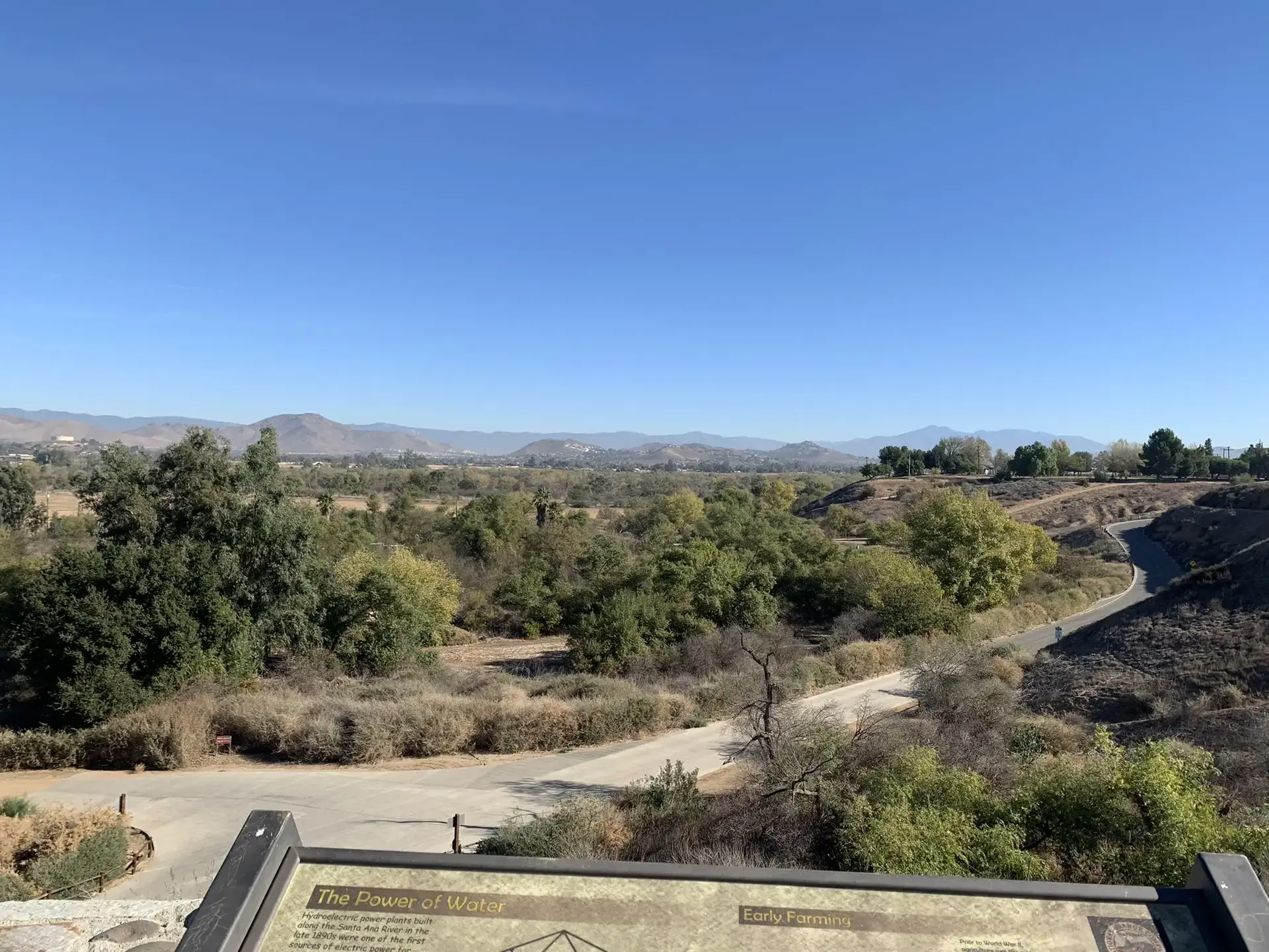An interpretive sign in the foreground overlooks a lush green valley with winding paths.