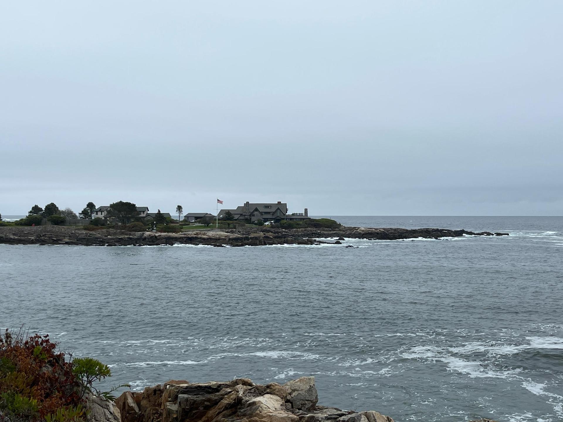 Distant island with buildings on a rocky coast under an overcast sky.