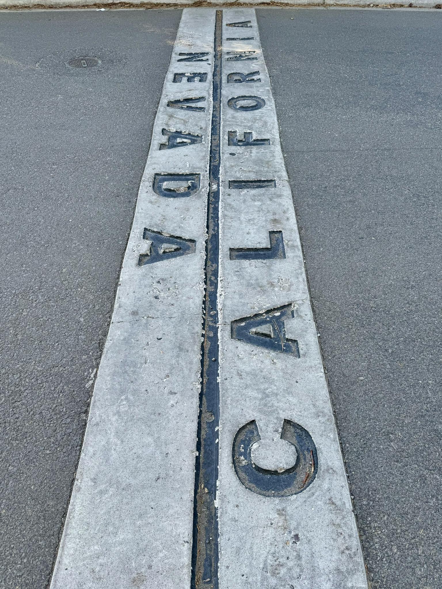 A concrete marker on asphalt, inscribed with "NEVADA" and "CALIFORNIA".