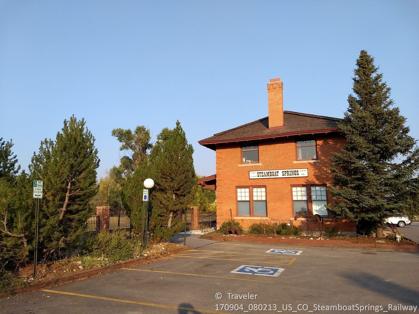 Brick building with a parking lot and tall pine trees under clear sky. - Rabbit Ears Pass