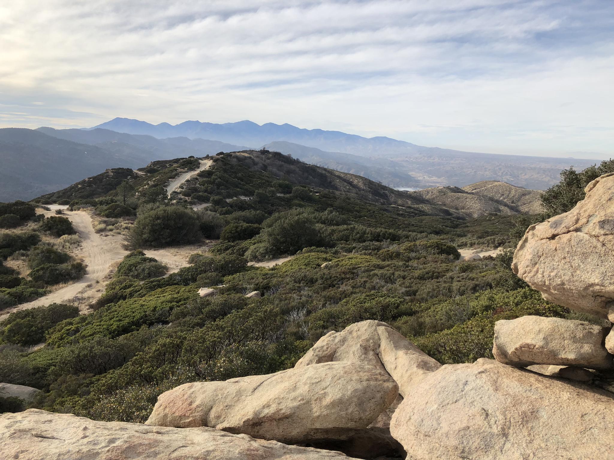Rocky foreground with a dirt path winding through hills under a cloudy sky.