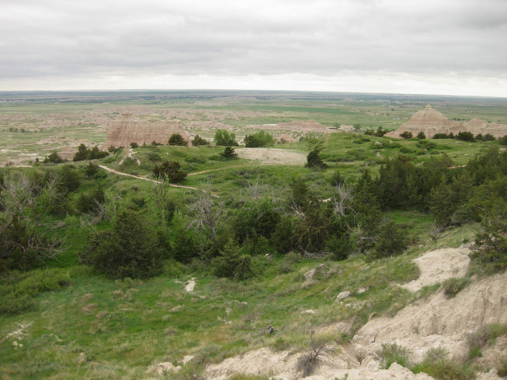 A wide view of a green, hilly landscape with distant rock formations under a cloudy sky.