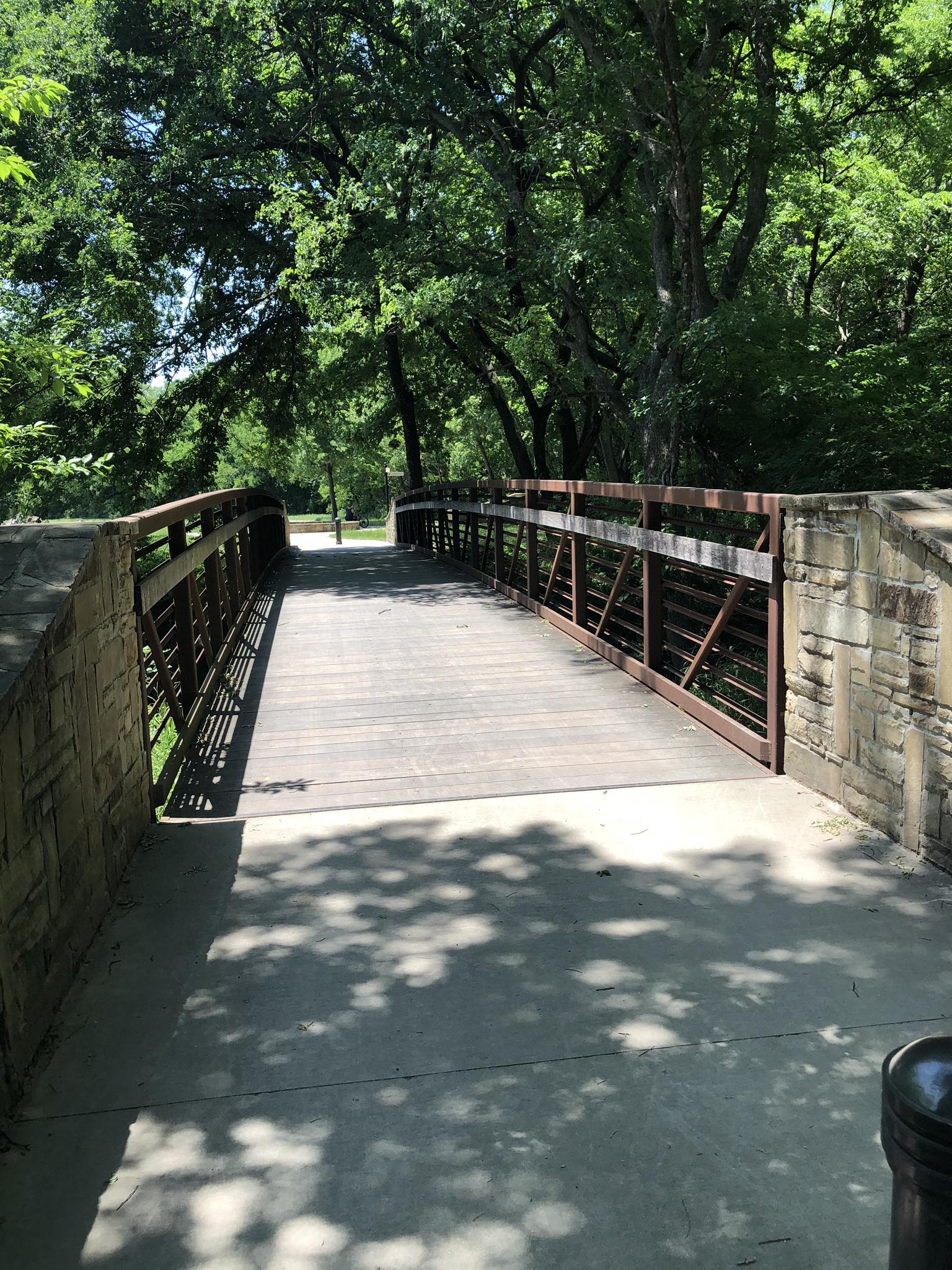 Sunny view of a wooden pedestrian bridge surrounded by lush green trees.