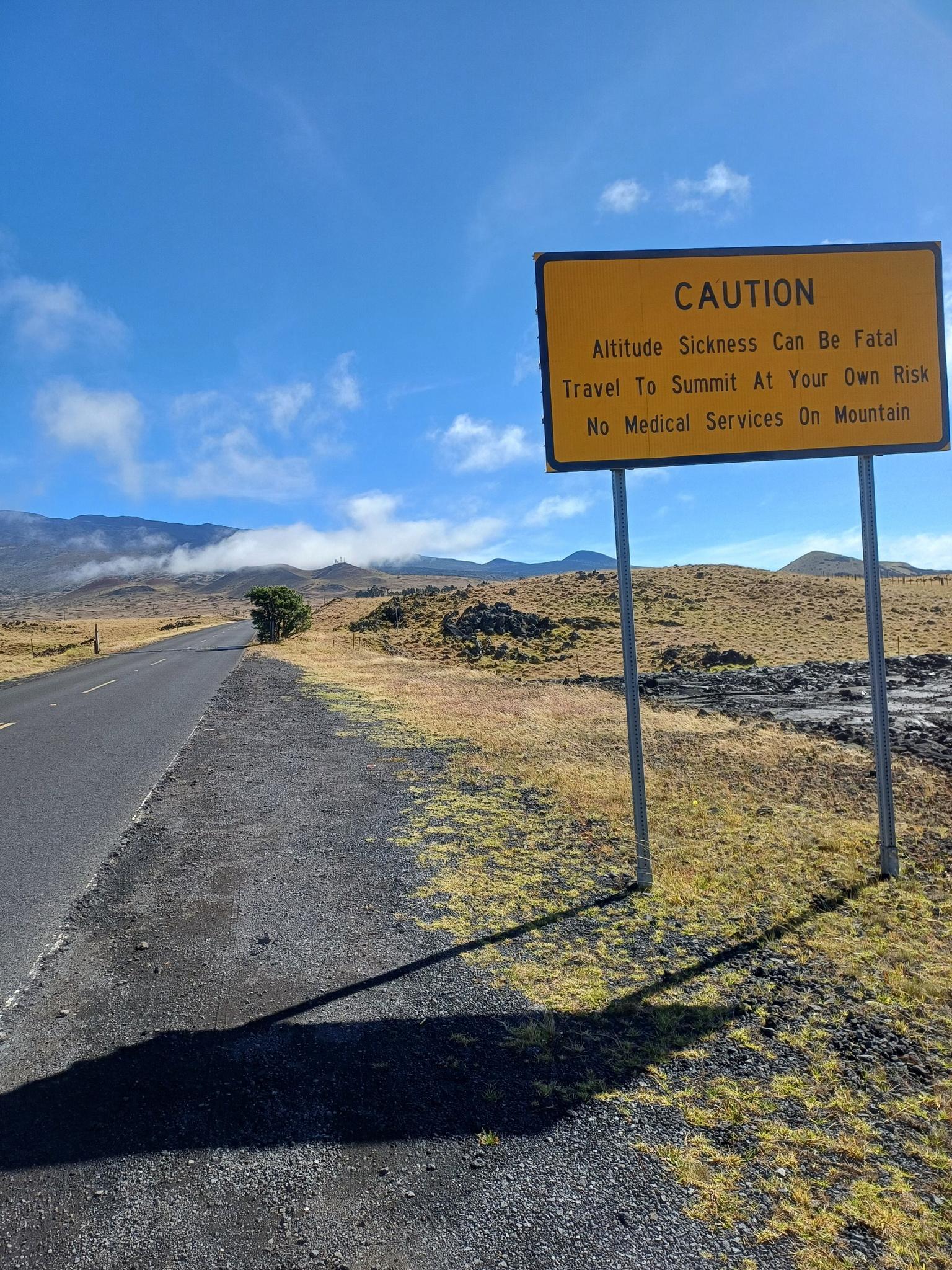 Yellow caution sign next to a road in a sunny, arid mountain landscape.