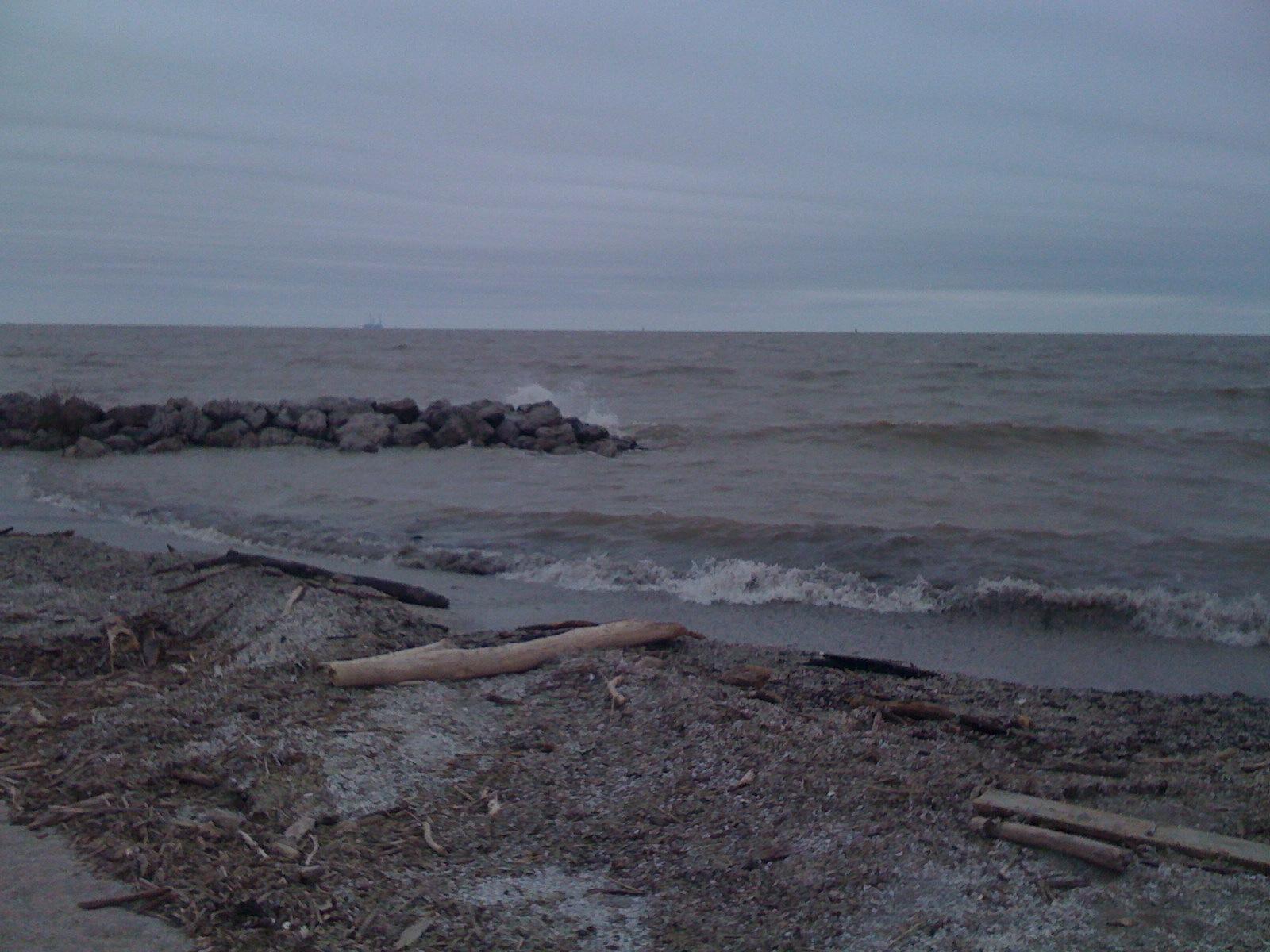 Dark, wavy water crashes against a rocky breakwater under an overcast sky.