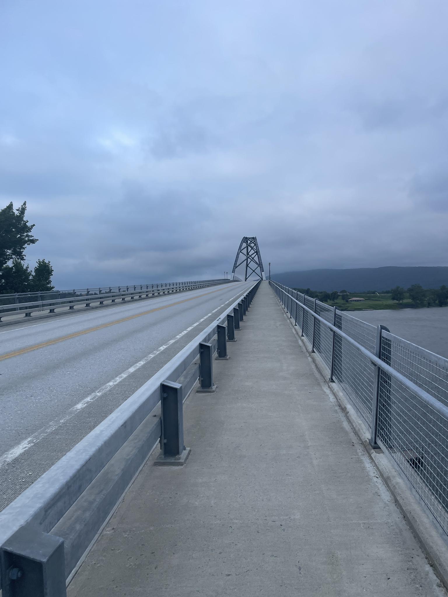 Overcast view of a long bridge with a road and pedestrian path over water.