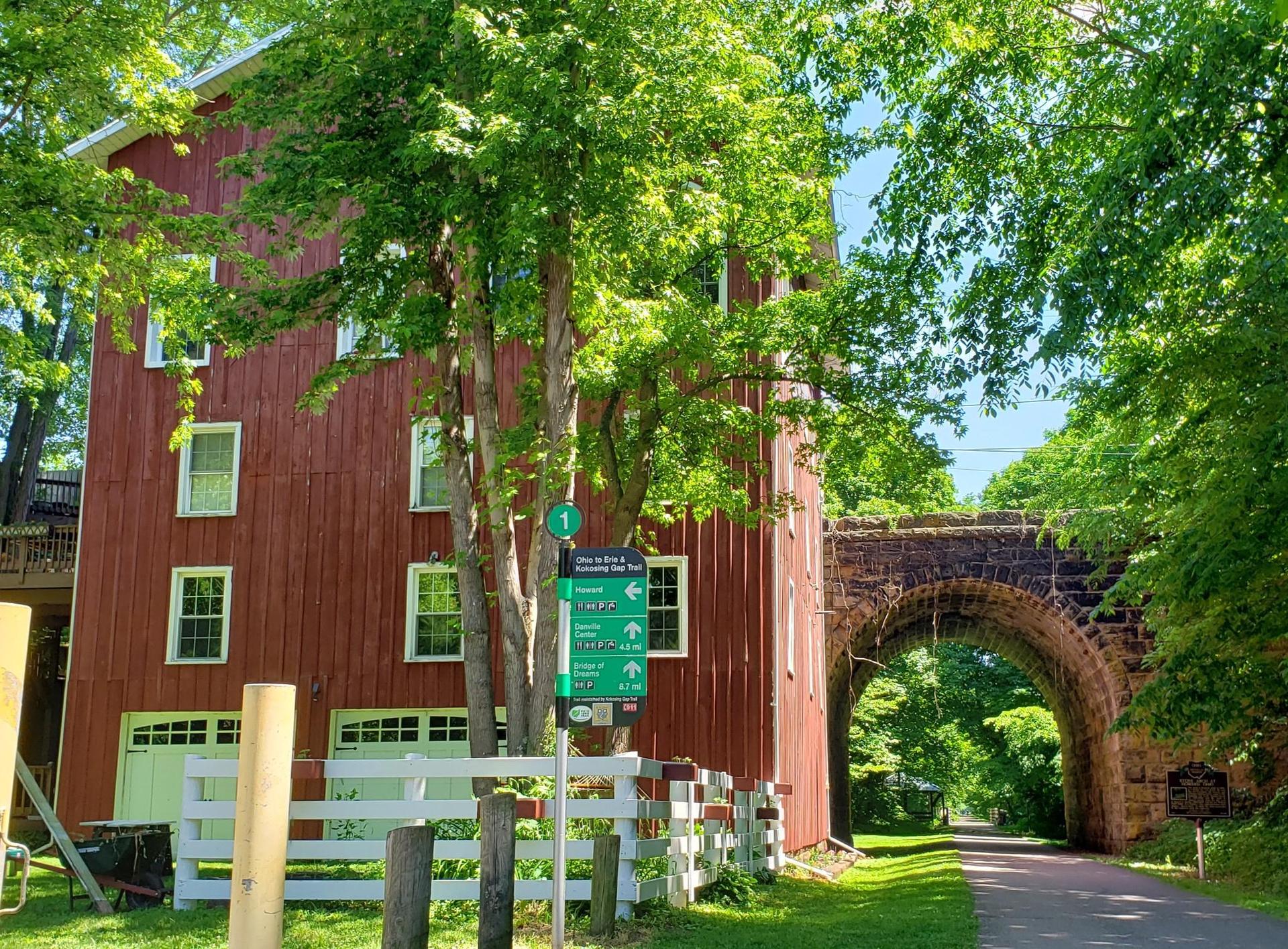 Red building next to a stone archway over a path, surrounded by trees.