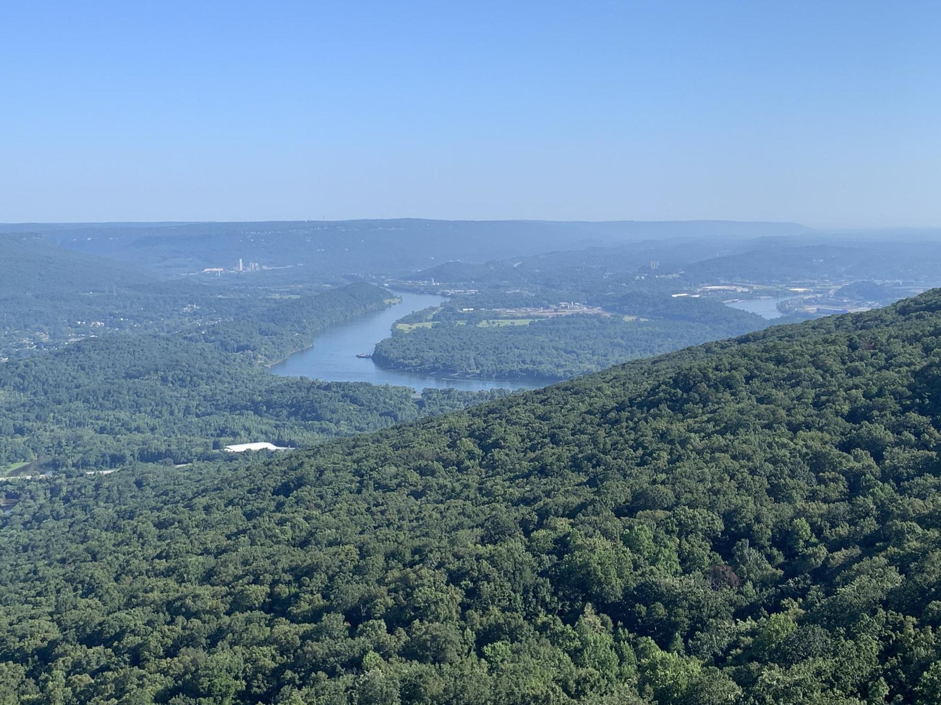 Expansive view of a forested valley with a winding river under clear sky.