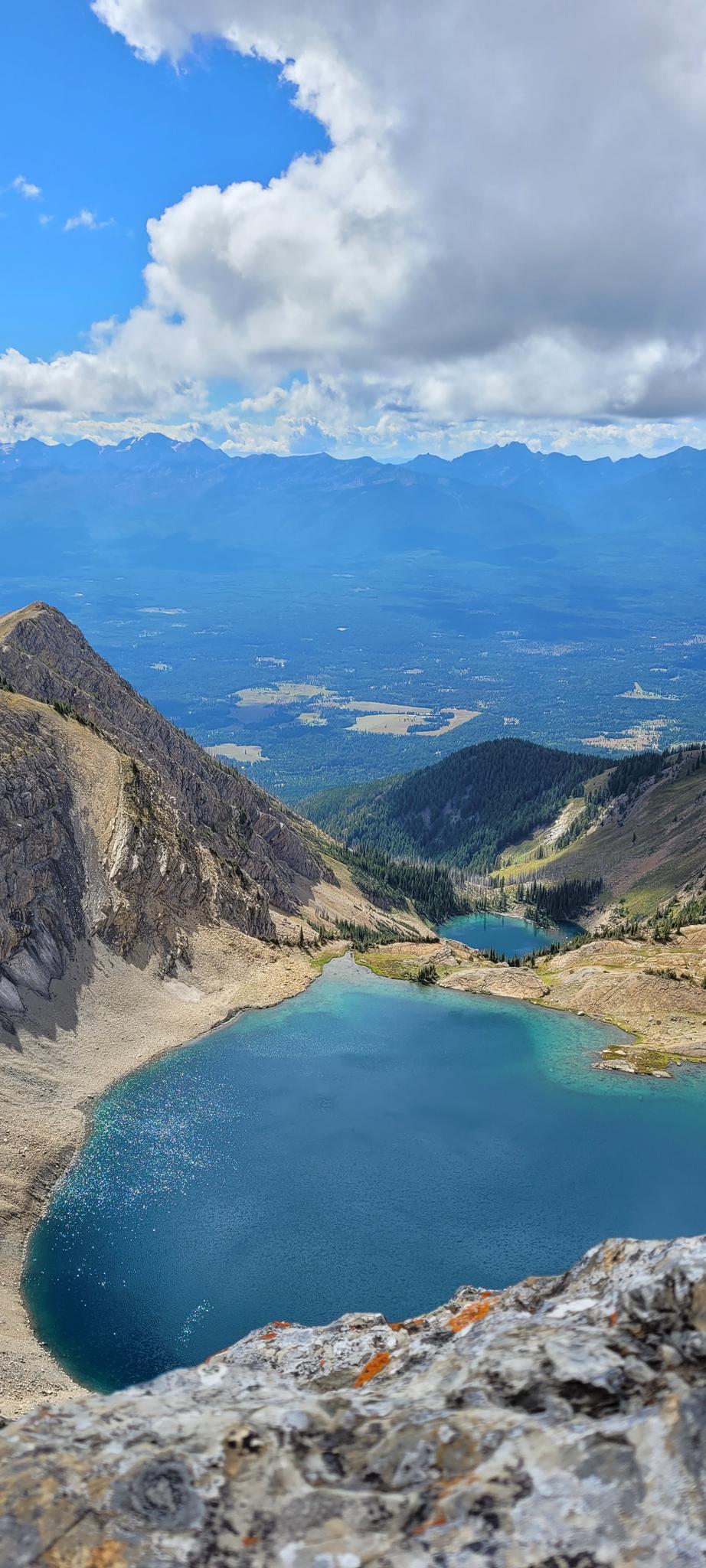 Vertical view of a bright blue mountain lake nestled among rocky slopes under a cloudy sky.