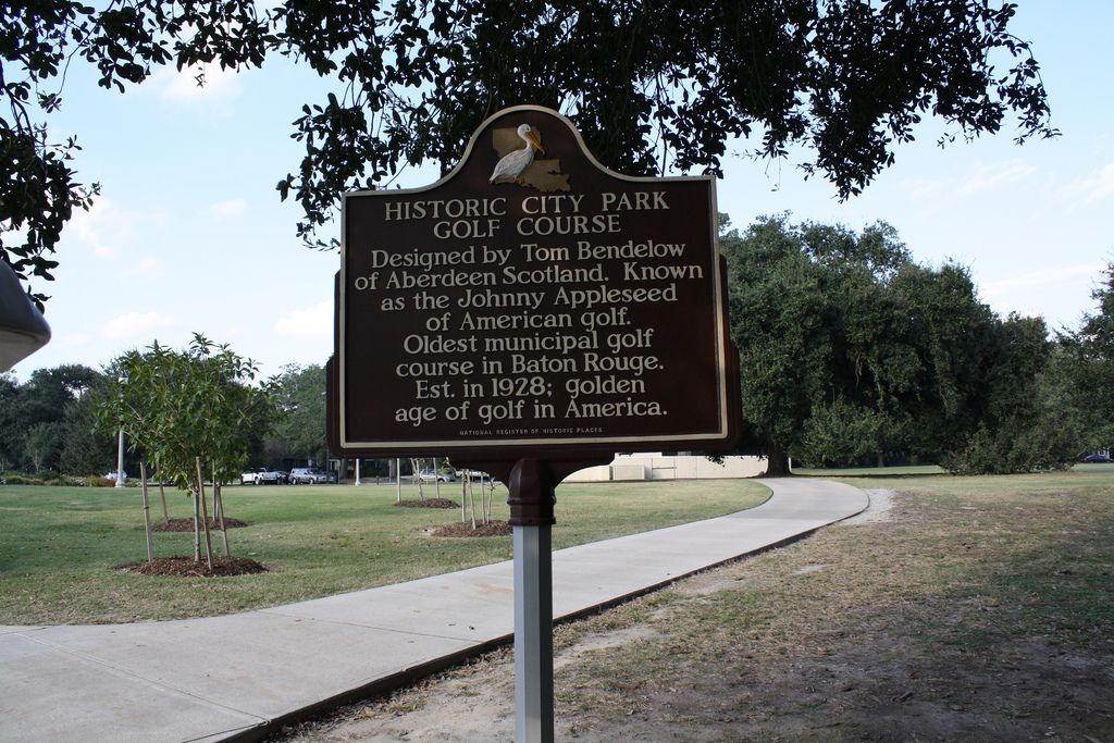 A brown historical marker stands beside a paved path in a sunny, grassy park. - City-Brooks Community Park loop from Baton Rouge Community College