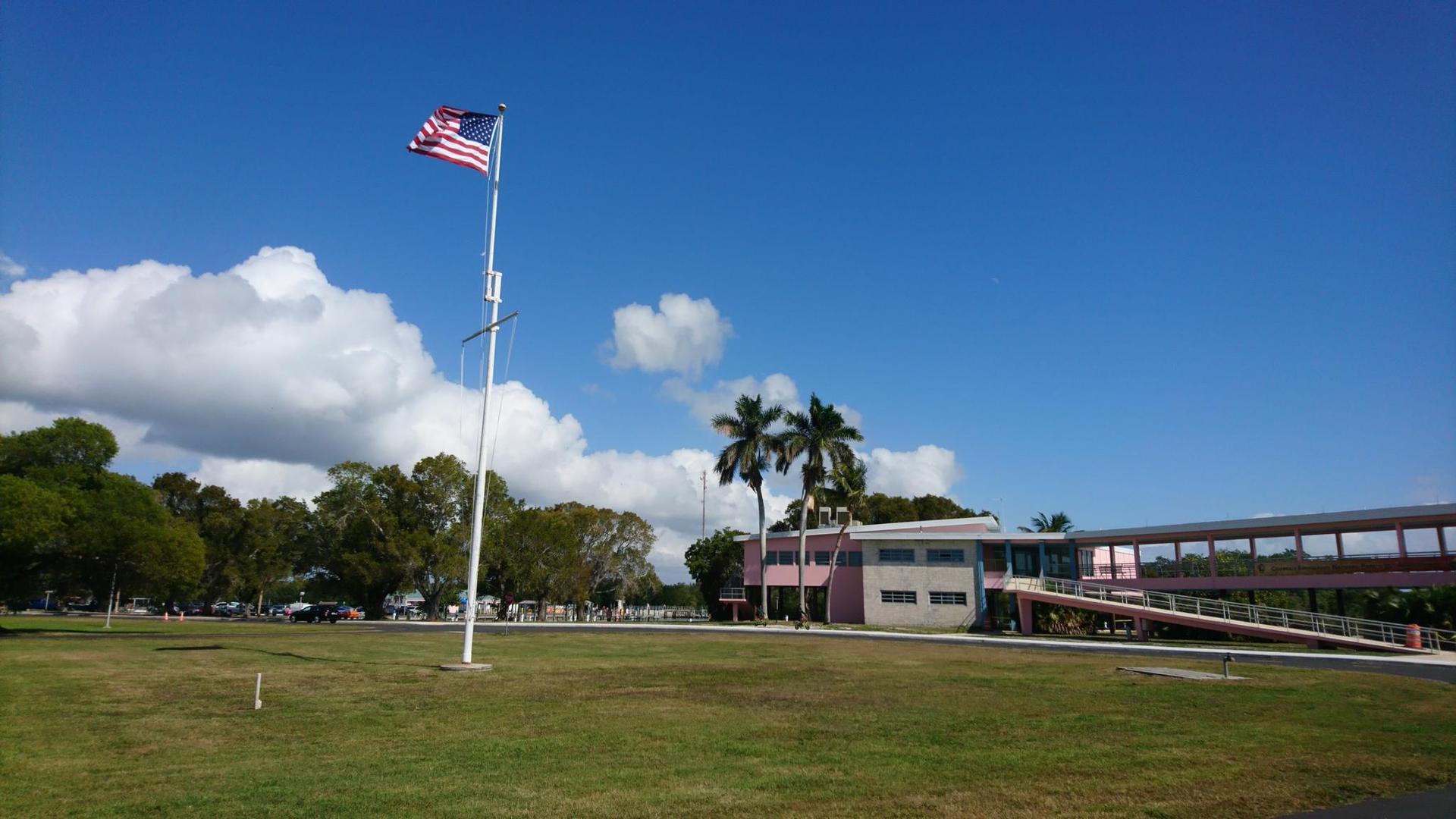 American flag waves proudly over a green field and building on a sunny day.