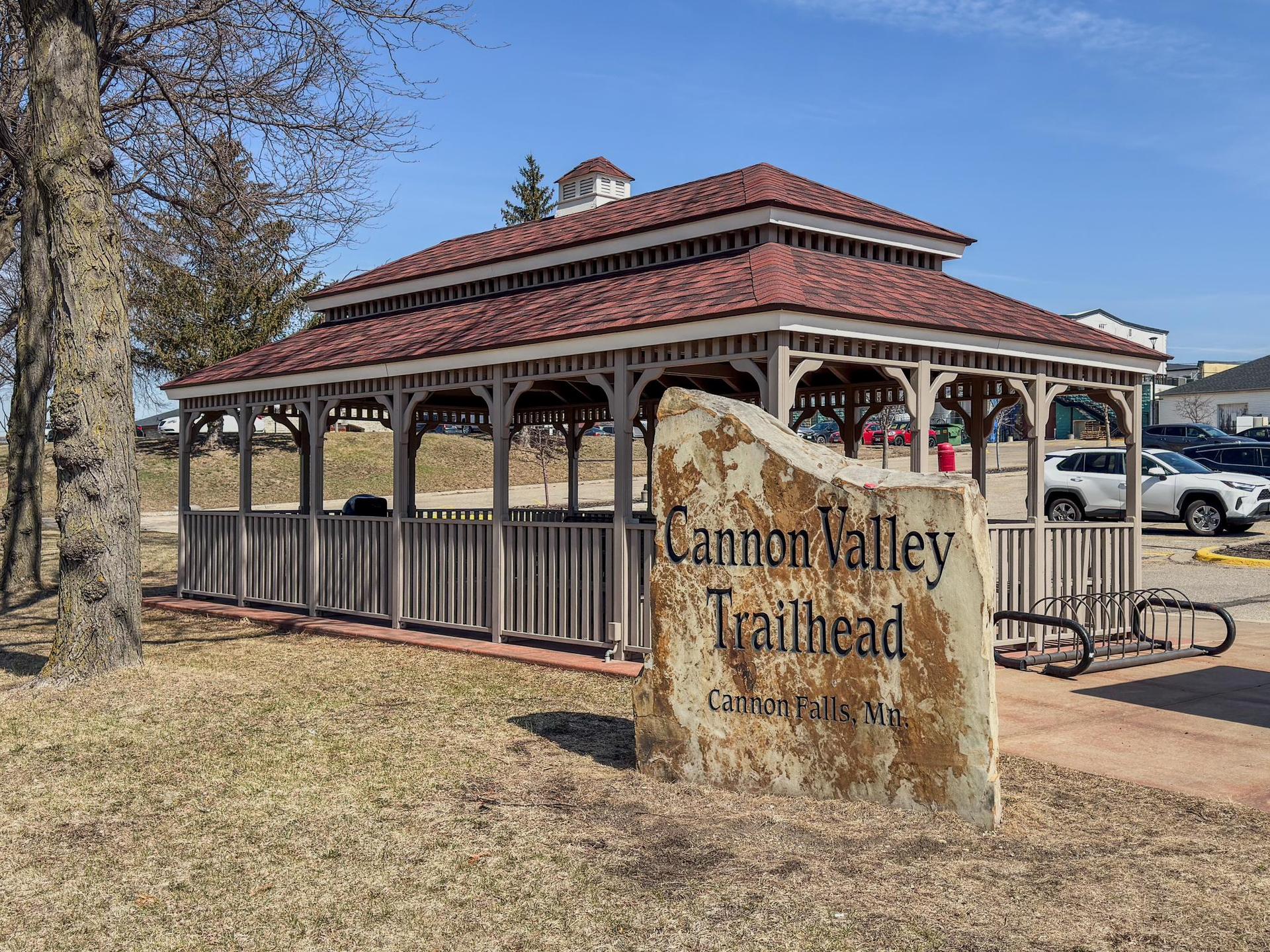Large wooden gazebo next to a stone sign on a sunny day.