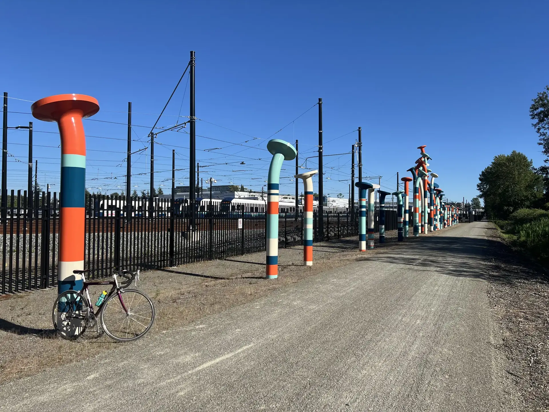 Colorful art pillars line a gravel path with a bicycle on a sunny day.
