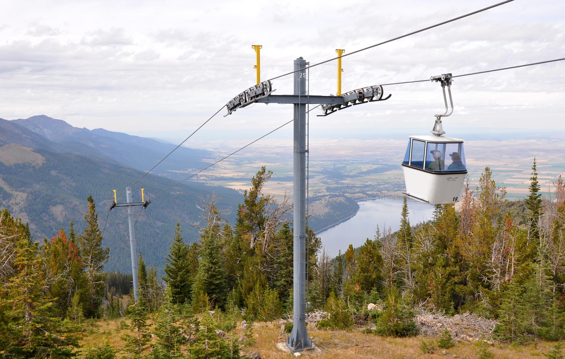 Gondola cabin with people ascending a mountain over a river valley.