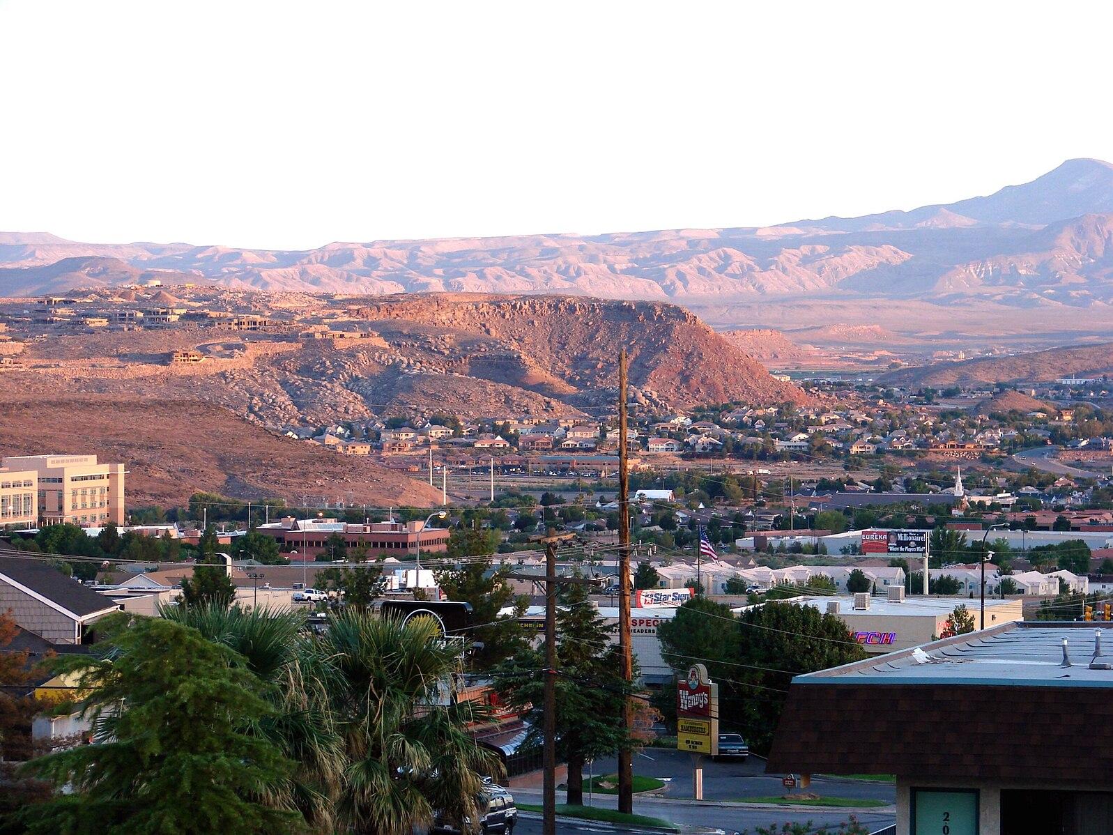 Cityscape with buildings and roads, surrounded by arid mountains at dusk.