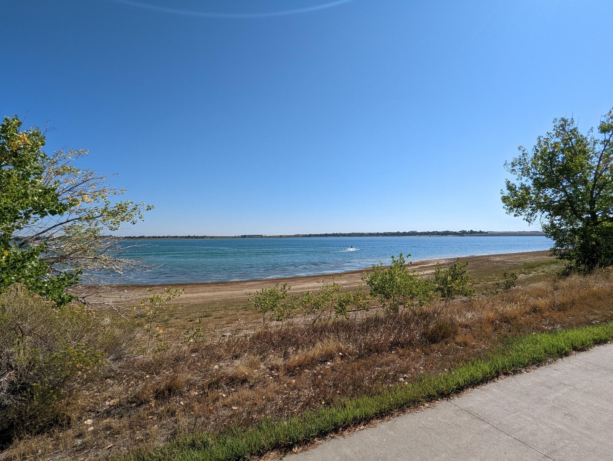 Expansive blue lake with a dry shoreline under a clear sky.