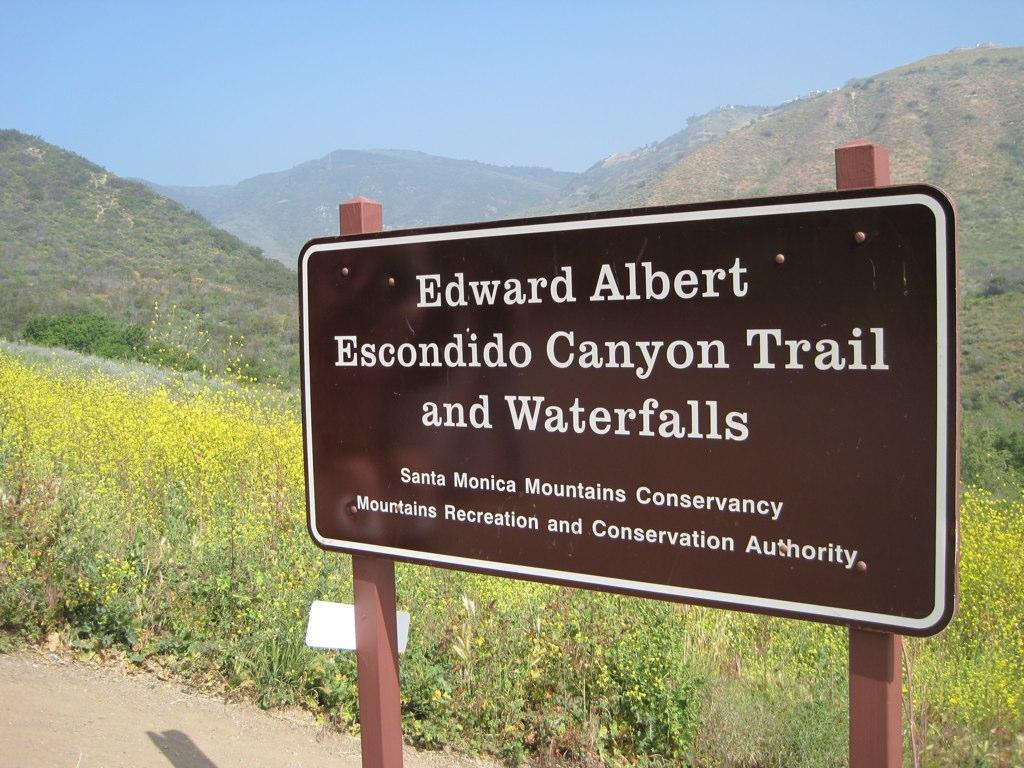 A brown park sign stands against sunny, grassy hills with wildflowers.