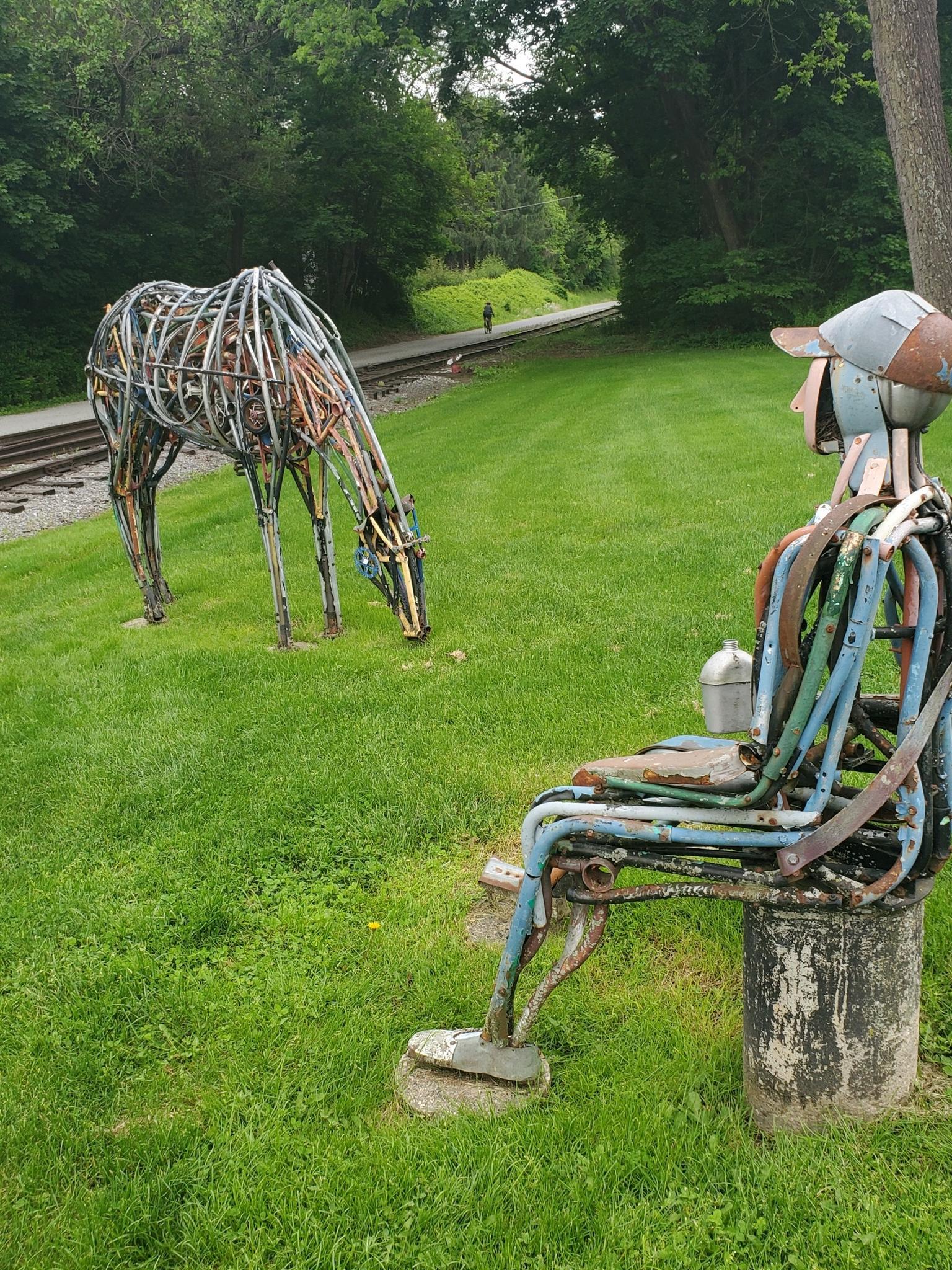 Metal sculptures of a person and a deer on a sunny grassy field.