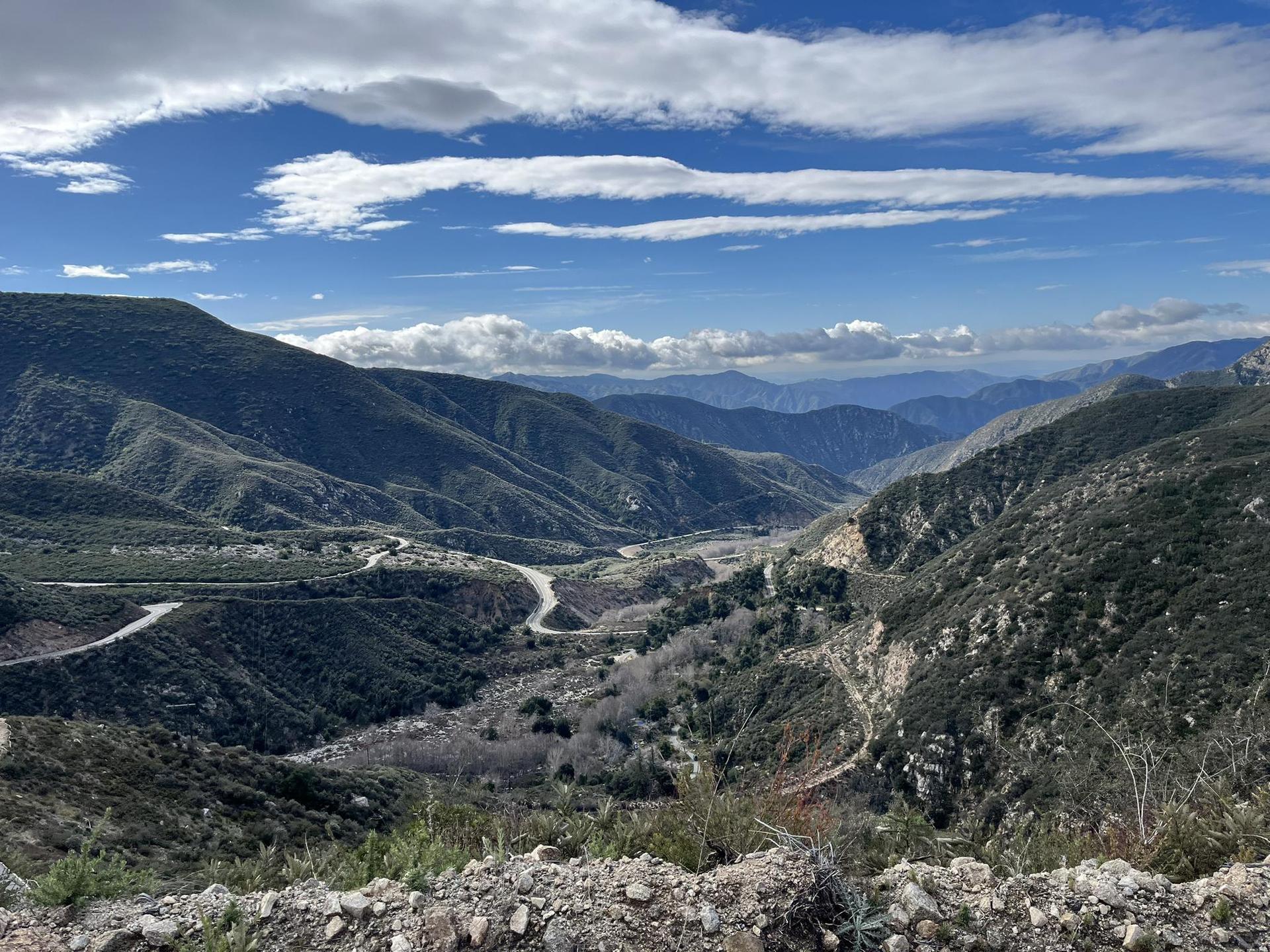Expansive view of green mountains and a valley under a partly cloudy sky.