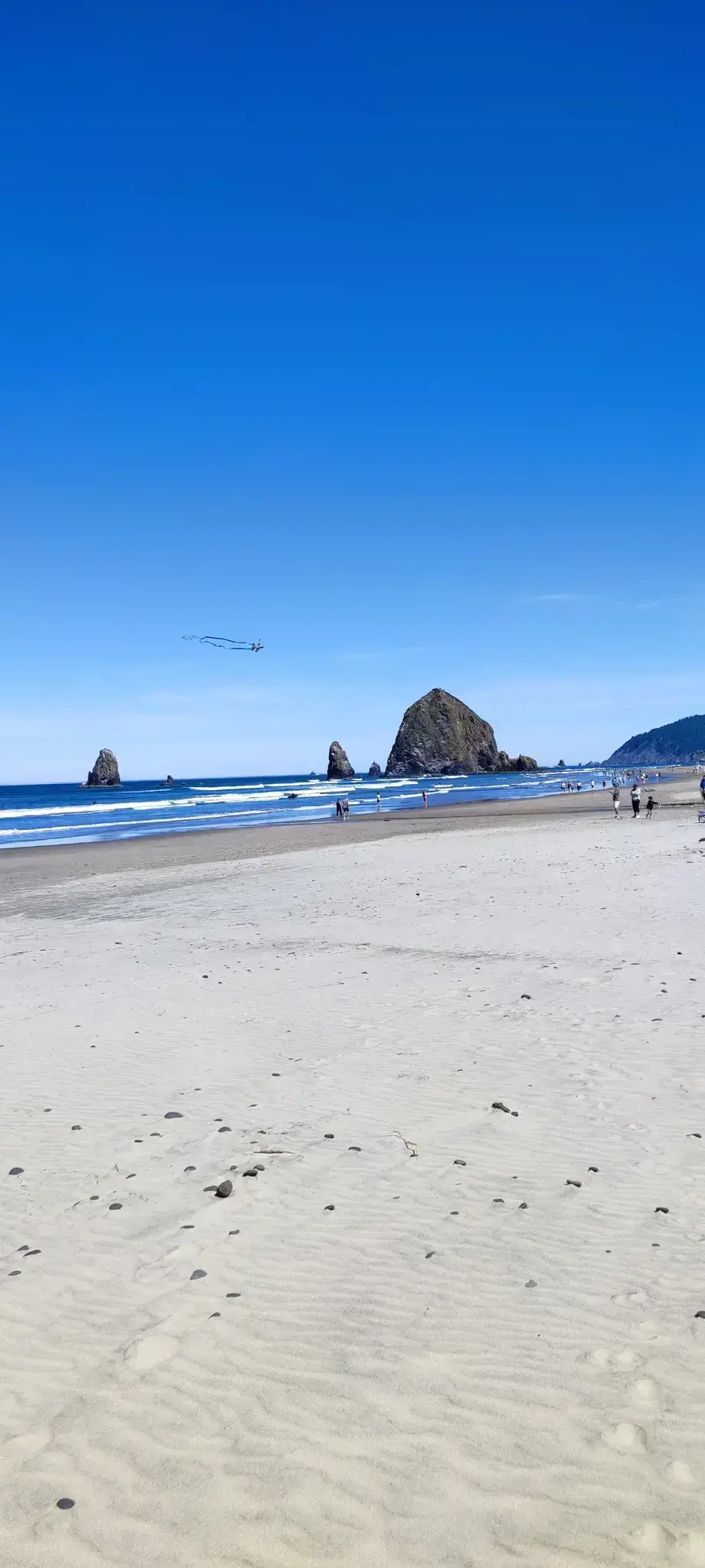 People walk on a wide sandy beach with distant sea stacks.