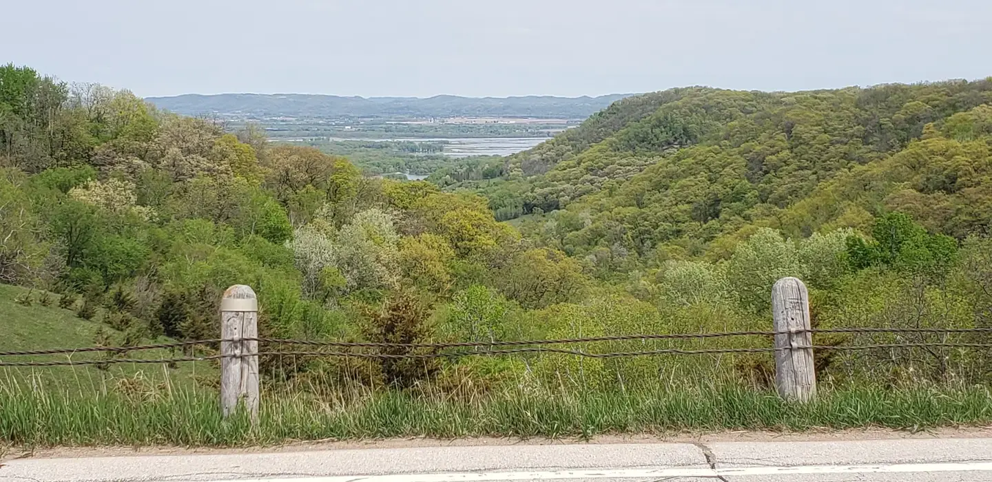 A scenic overlook of a green valley and distant river, framed by fence posts.