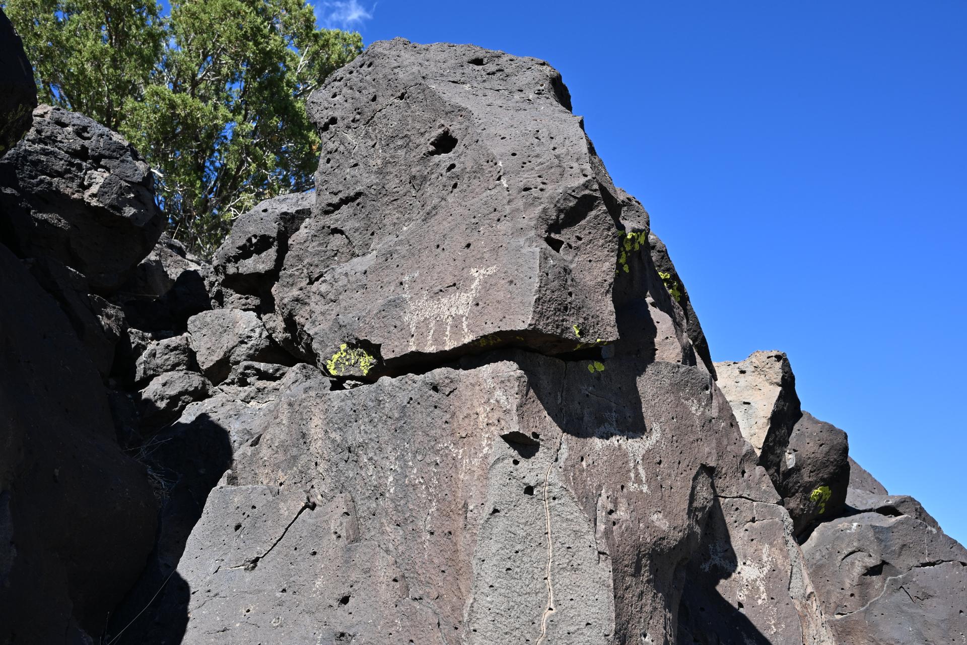 Large dark rock formation with ancient carvings under a bright blue sky.
