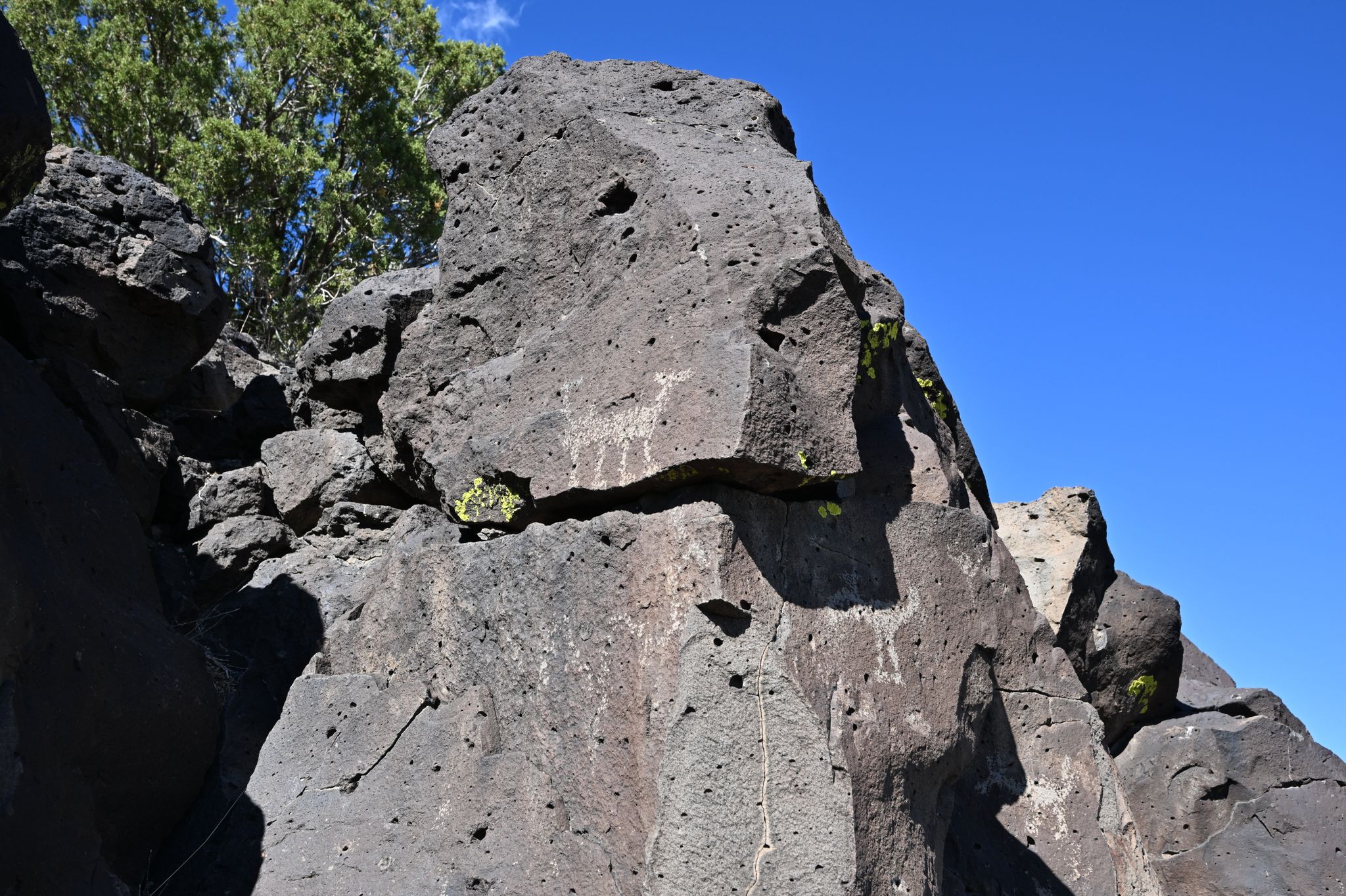Large dark rock formation with ancient carvings under a bright blue sky. - El Camino Real and Caja del Rio Loop