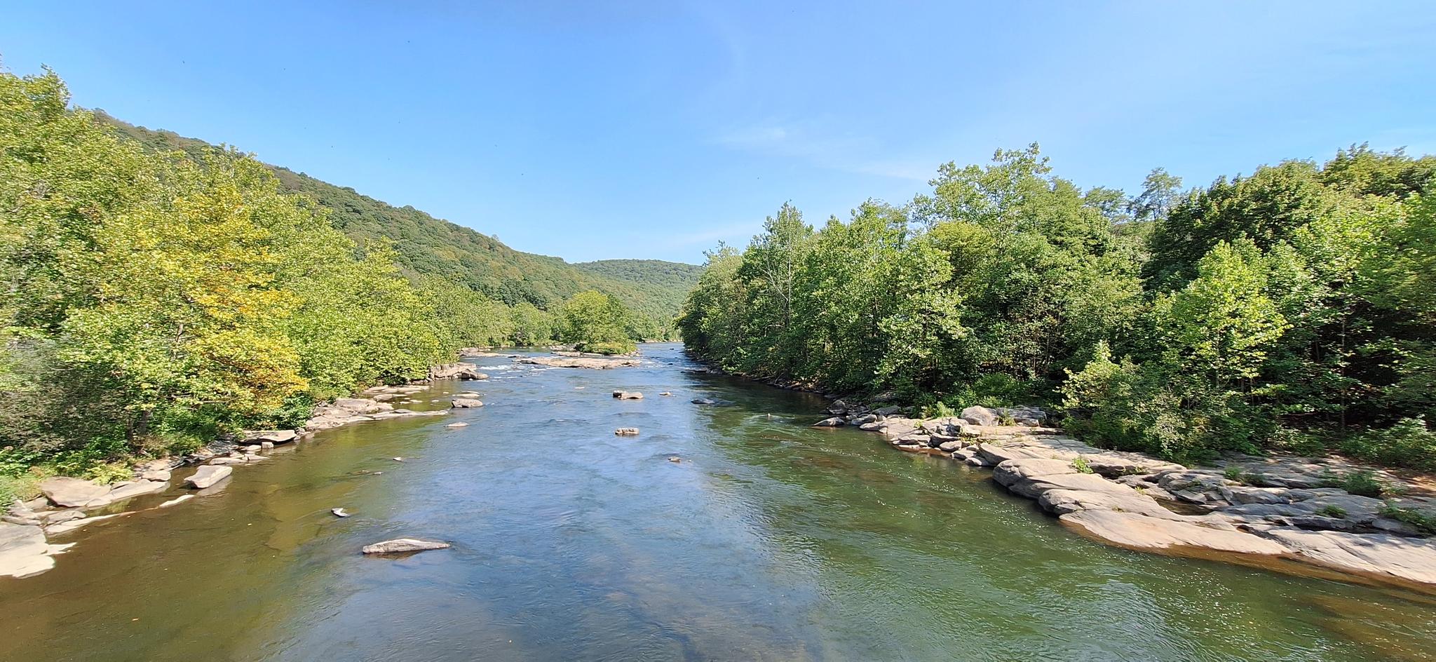 Wide river flowing between lush green forested hills on a clear day.